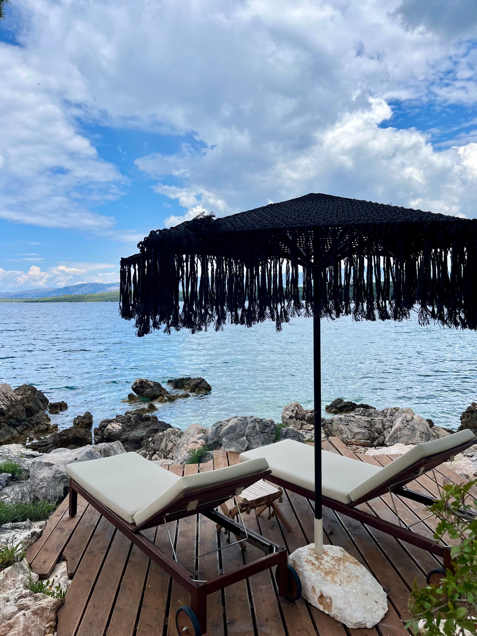 Lounge chair with an umbrella next to a body of water.
