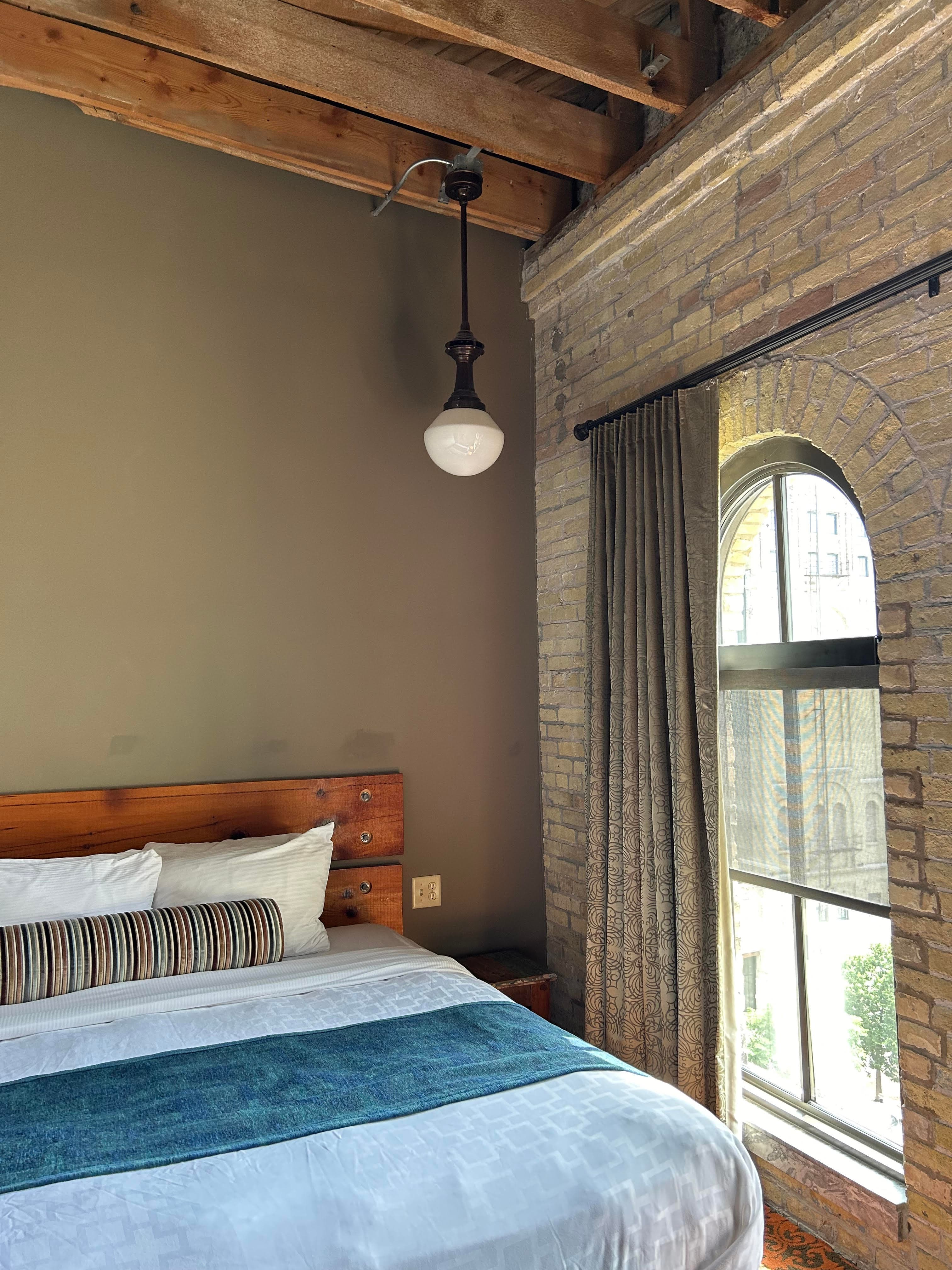 Patio dining tables sit under large umbrellas on a stone walkway under large green trees on a sunny day.