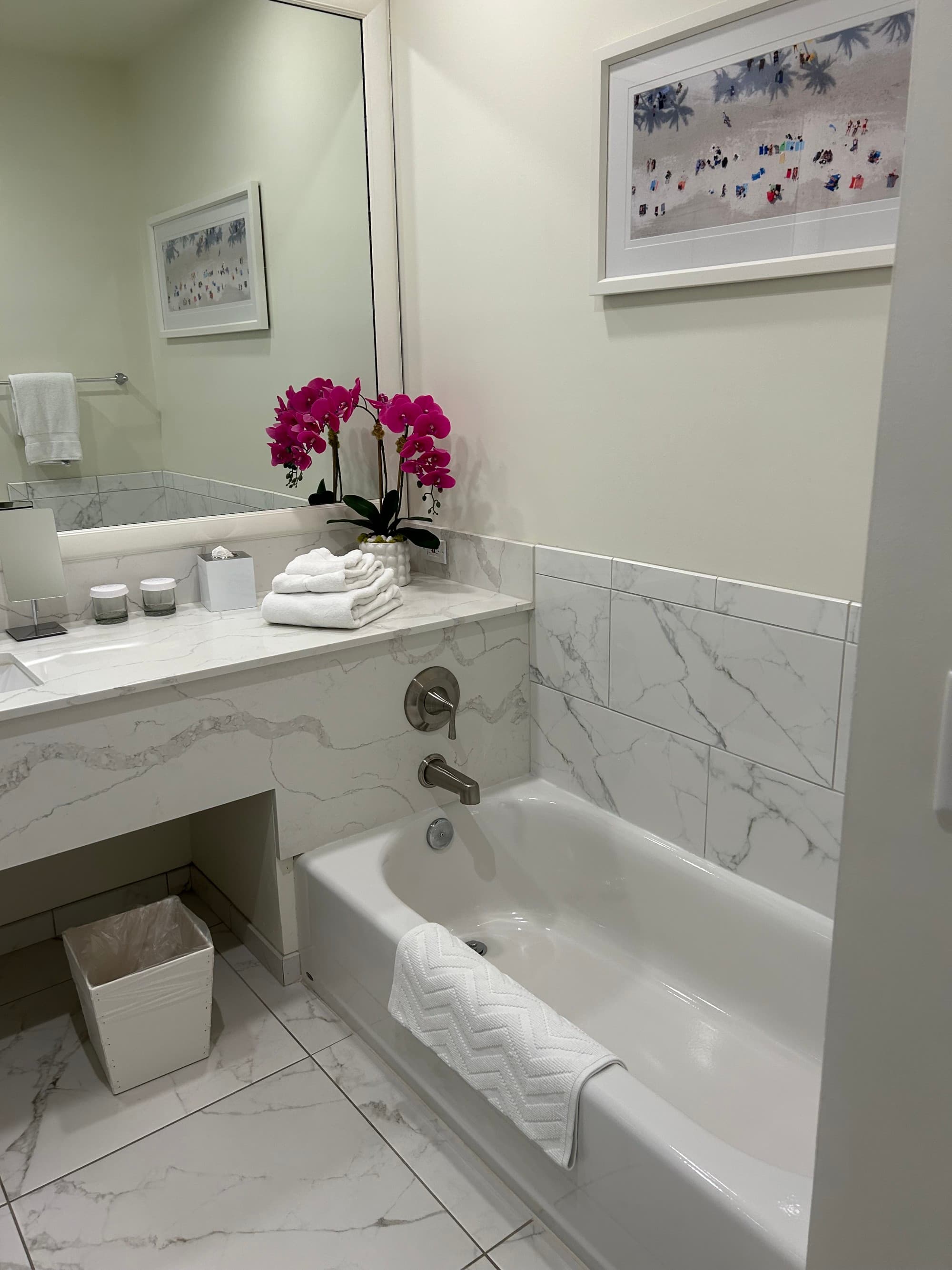 Marble bathroom with a bathtub and pink flowers on the counter.