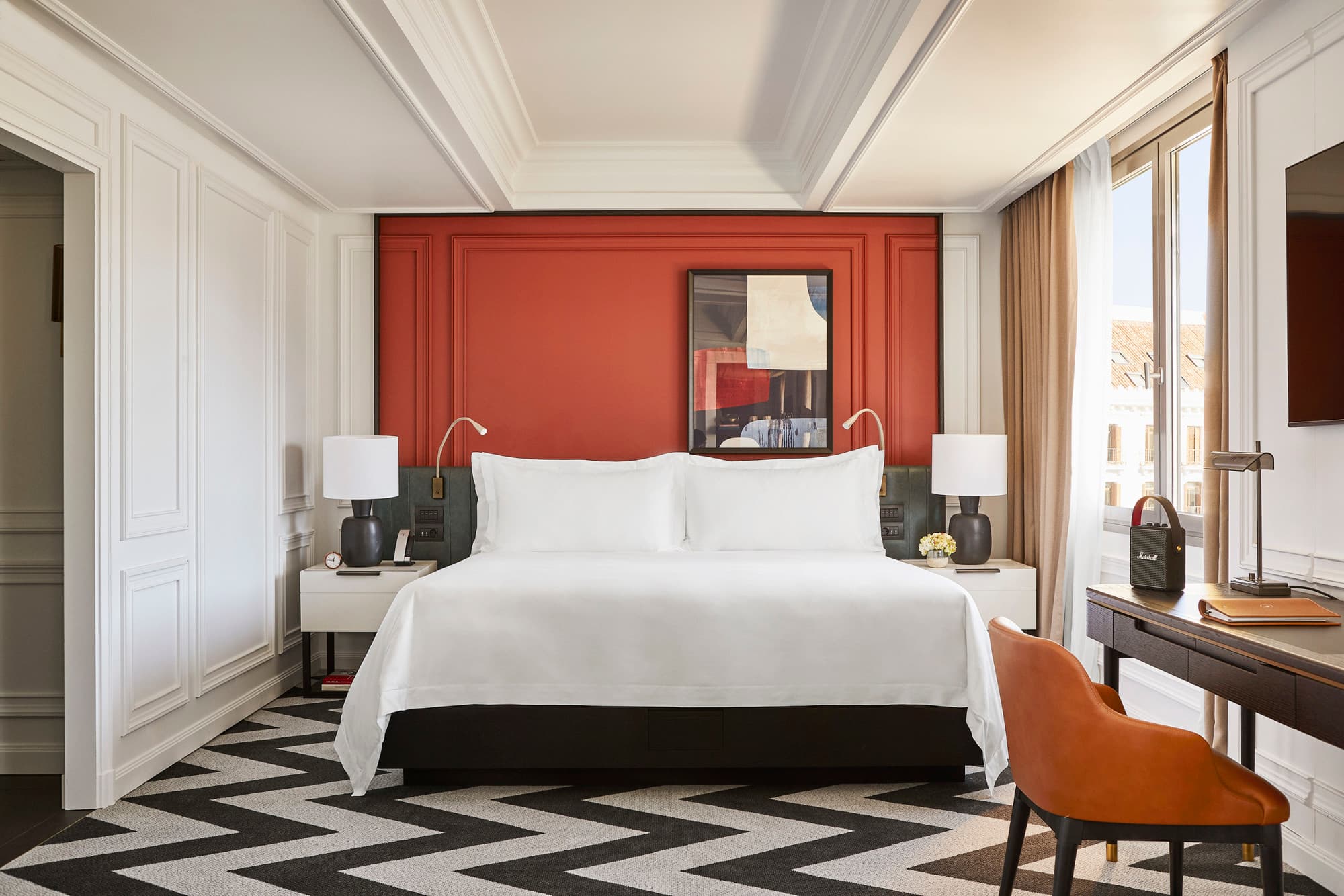 a white bed in front of an orange wall with a mirror