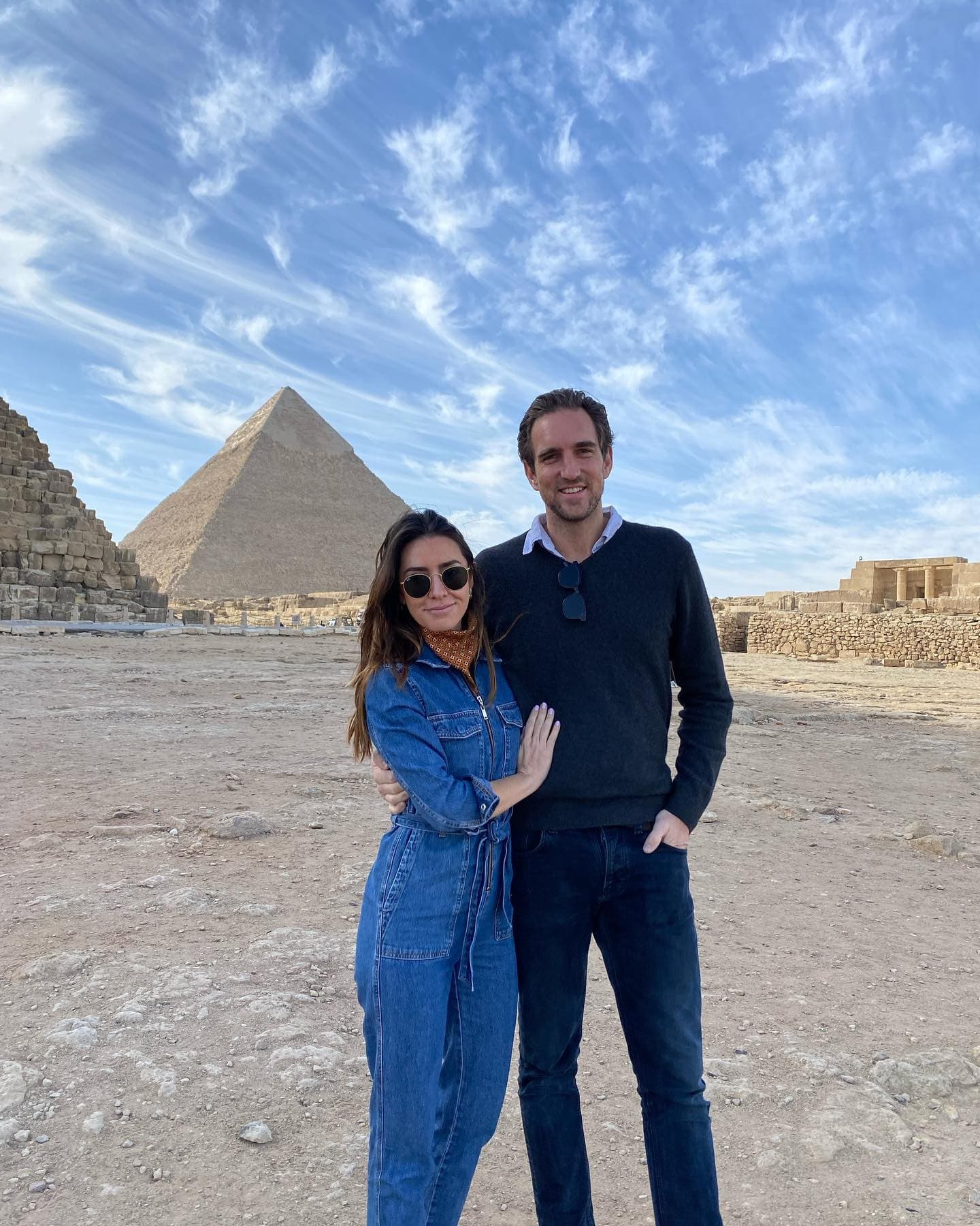 a man and a woman in a denim jumpsuit stand in front of the Egyptian Pyramids