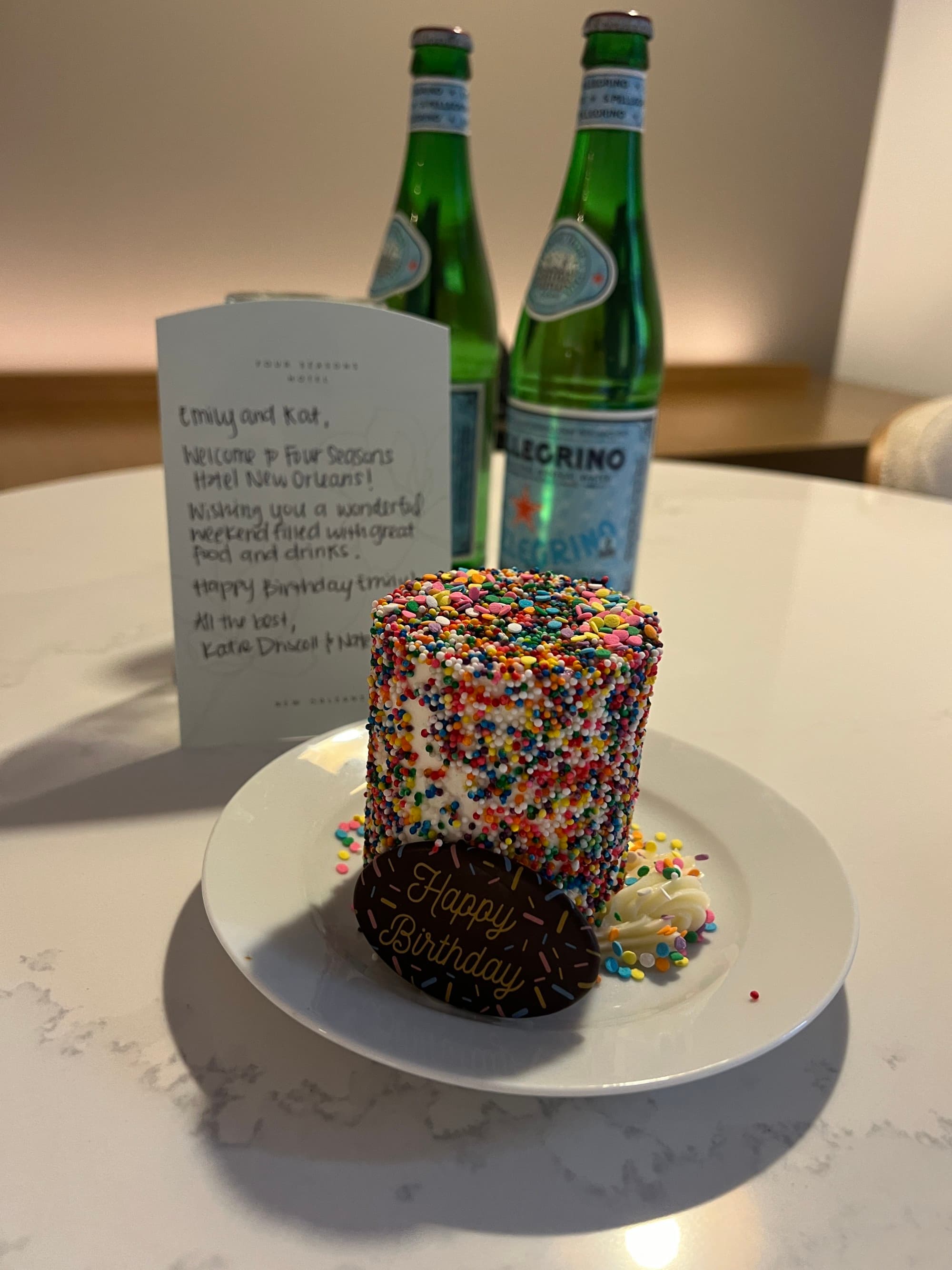 A view of a dessert covered in colorful sprinkles and two glass Pellegrino sparkling water bottles.