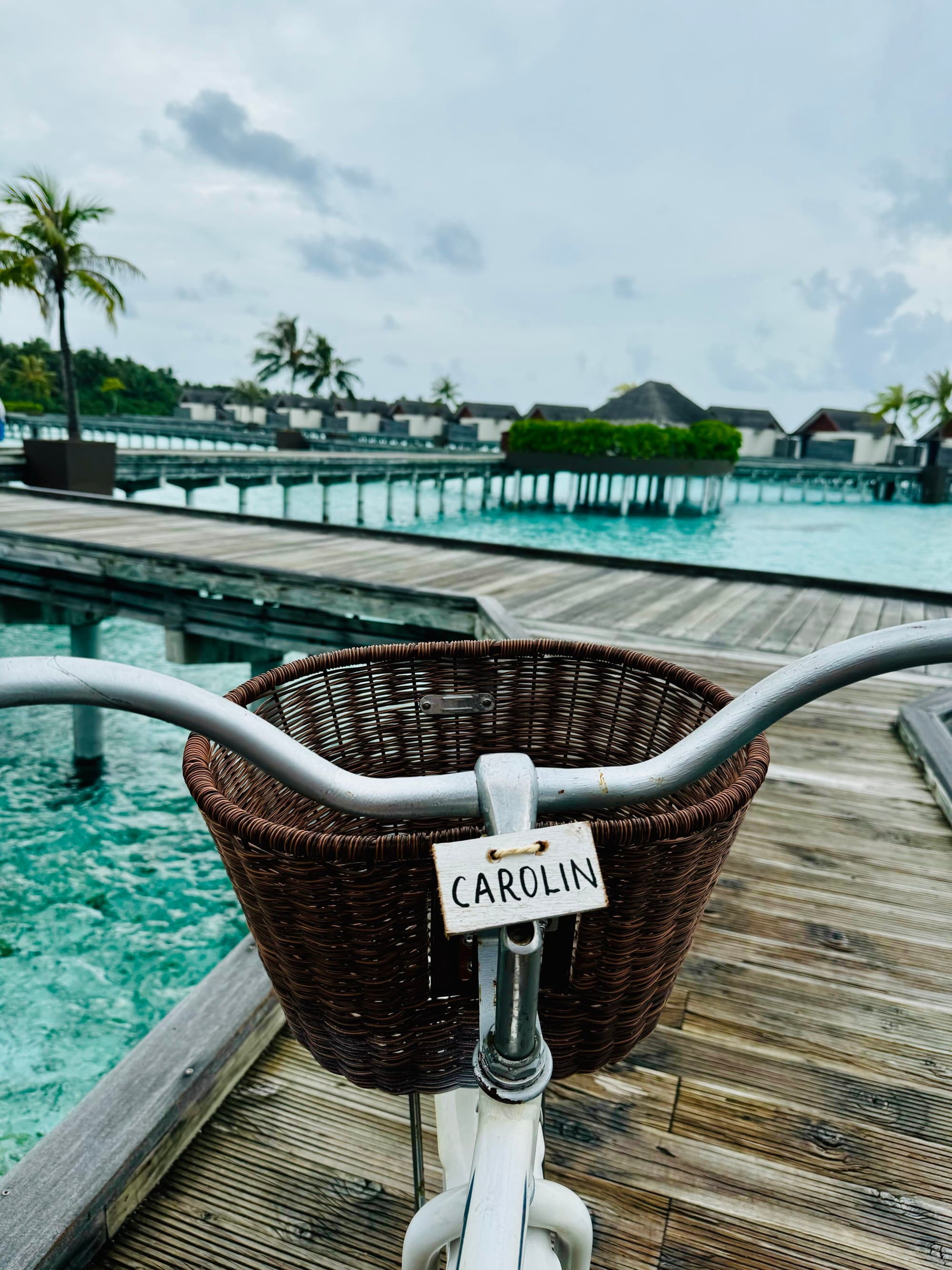 Bike with a basket on a boardwalk above blue ocean water.