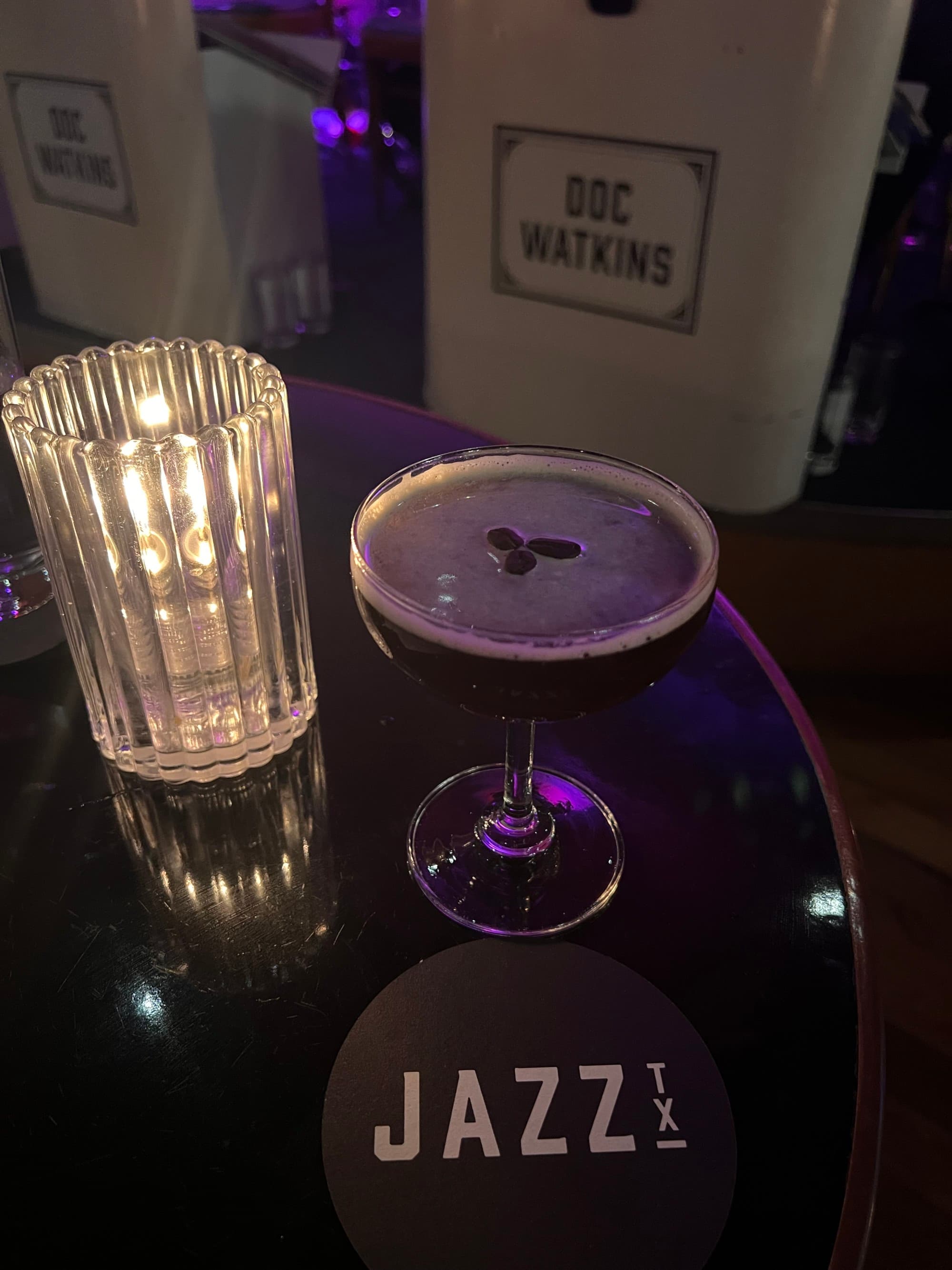 A cocktail on a table next to a candle