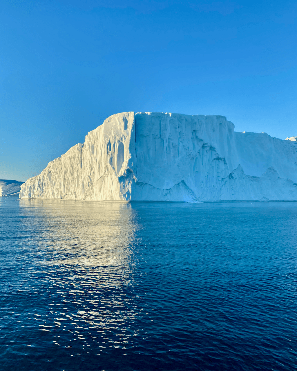 A large white iceberg in the ocean against bright blue sky in Ilulissat, Greenland