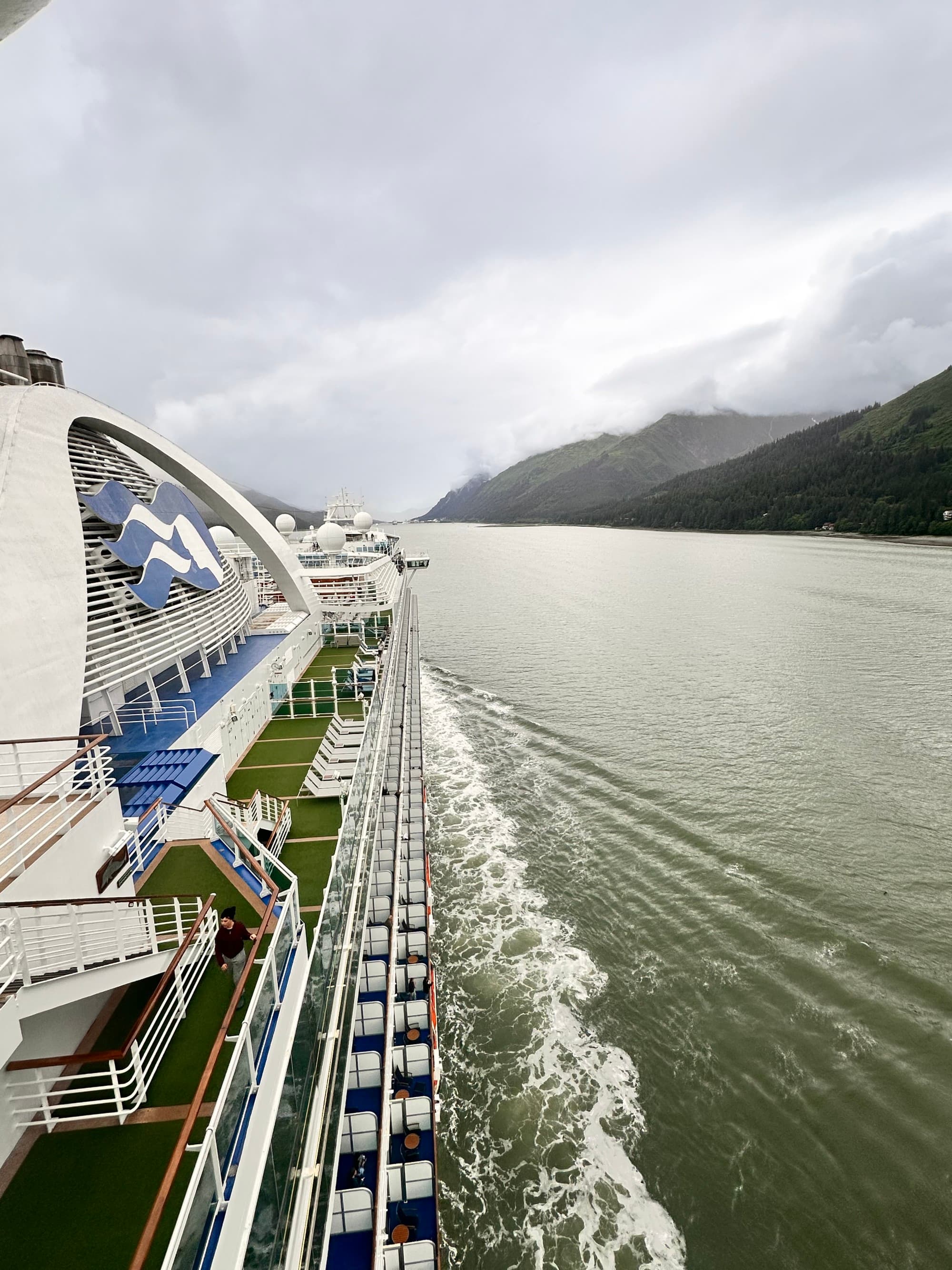 The side of a cruise ship with lots of balconies and a large wake.