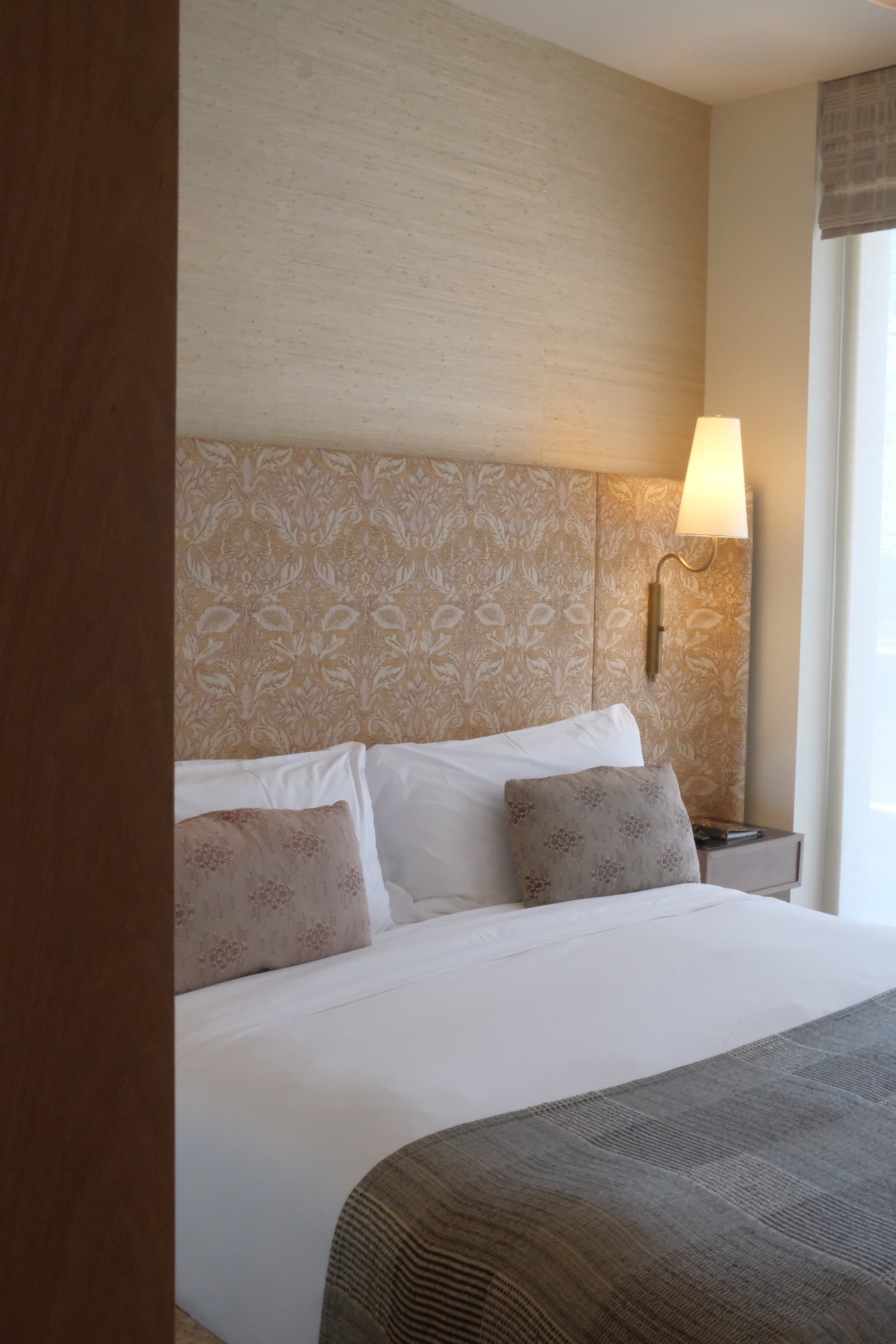 The king sized bed in the Premier Room with premium Italian linen and custom throws by Kelly Wearstler near a window on a clear day.