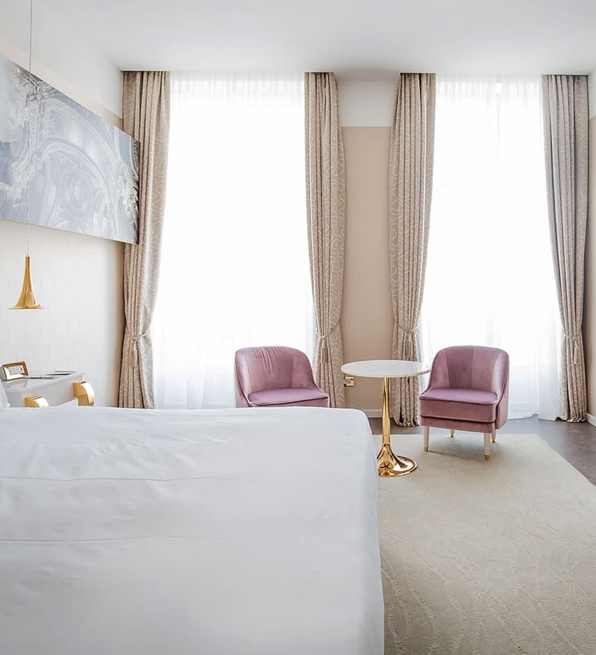 A photo of a hotel room showing the corner of a bed and two purple chairs