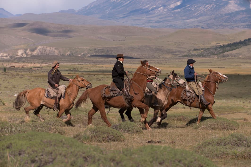 four horses and riders in a valley with mountains in the background