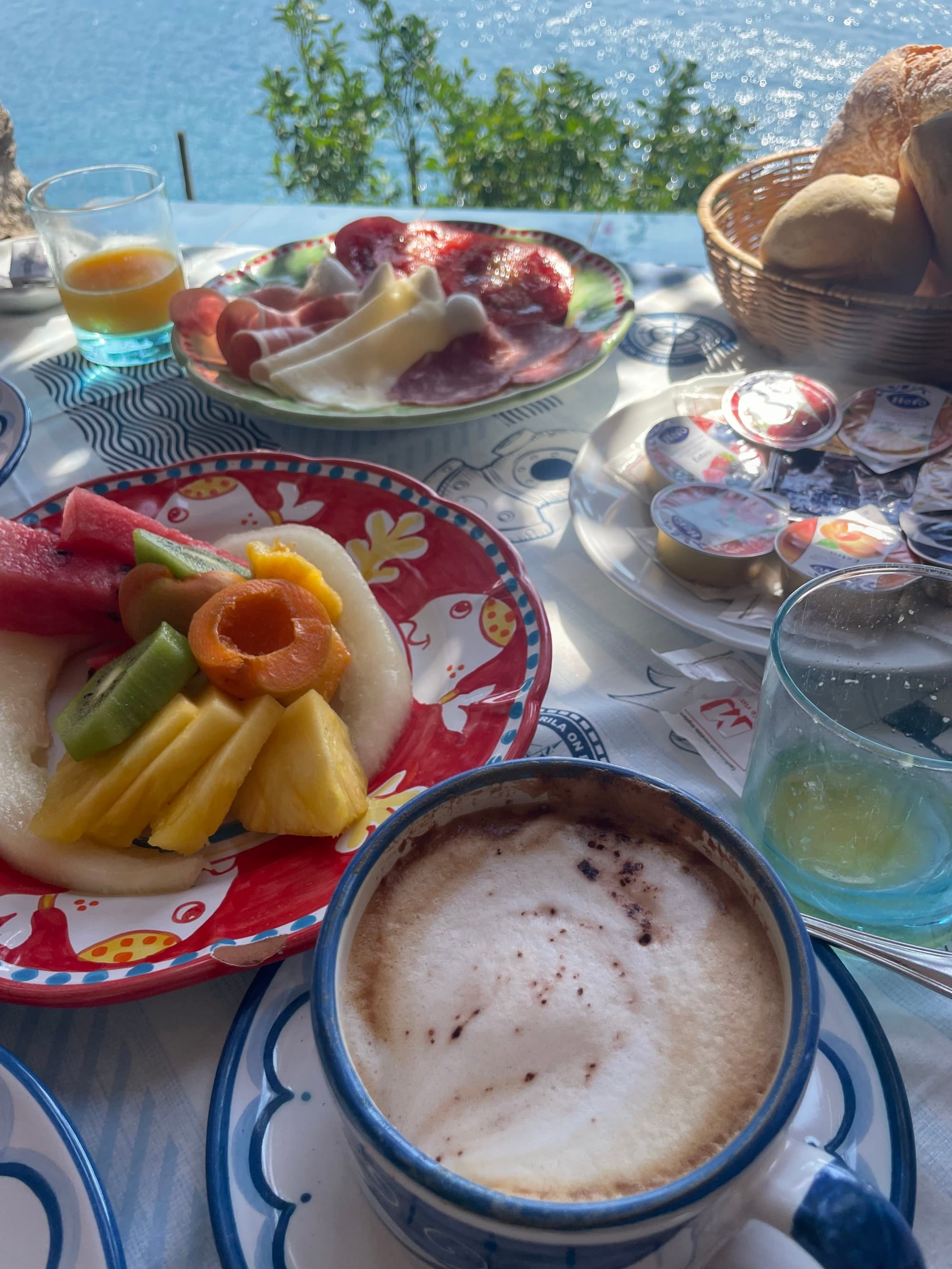 Multiple plates of food on an outdoor table with a view of the water in the distance