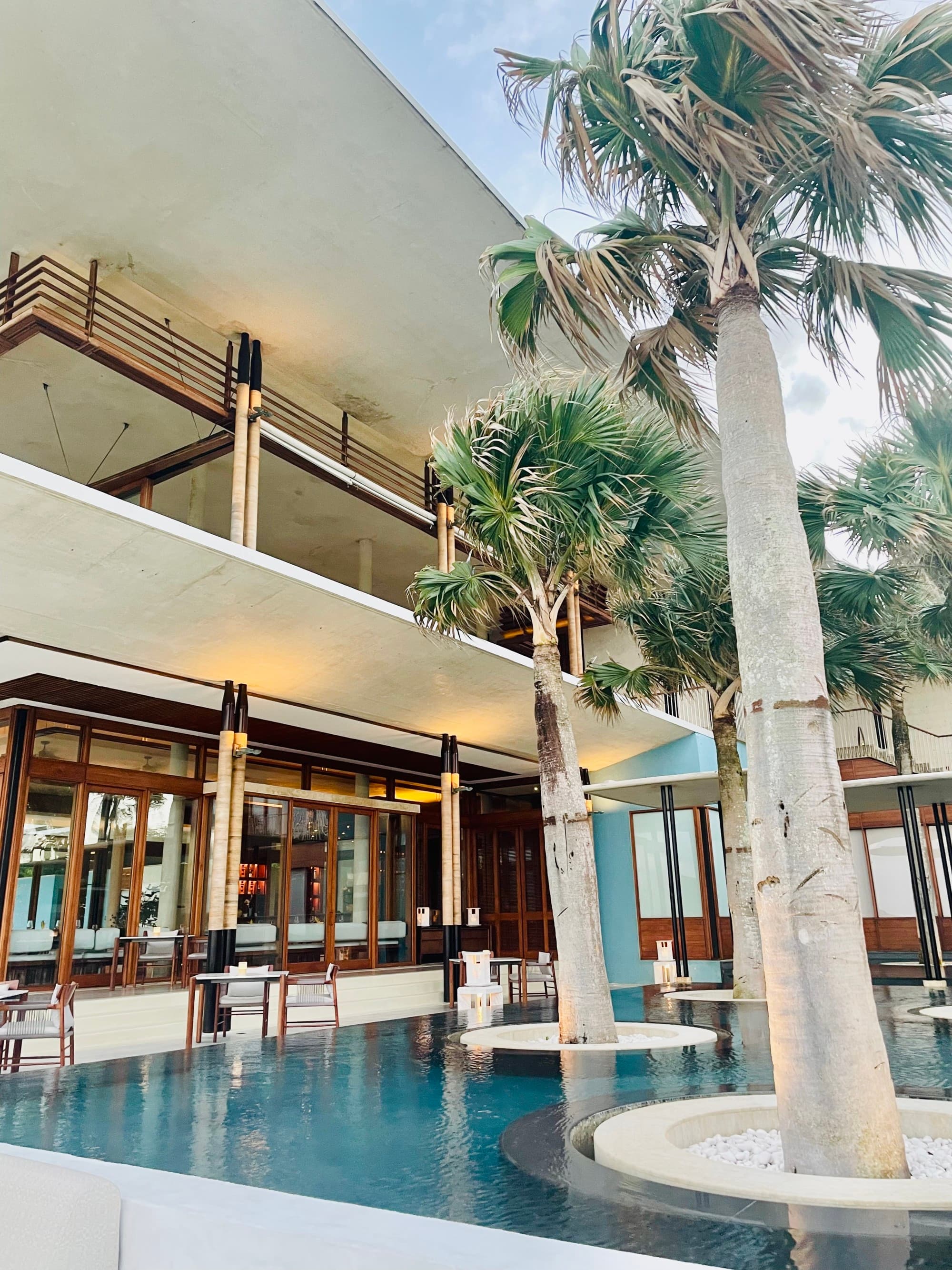 A bar in an open-air hotel lobby with palm trees.