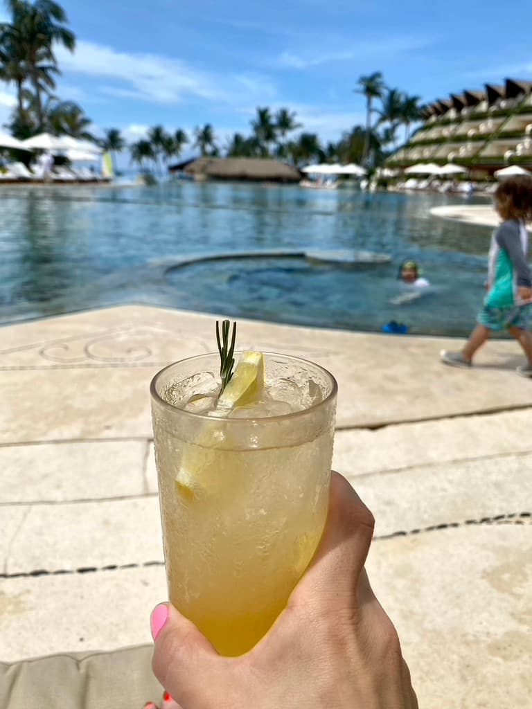 A person holding up a drink glass next to an outdoor pool area