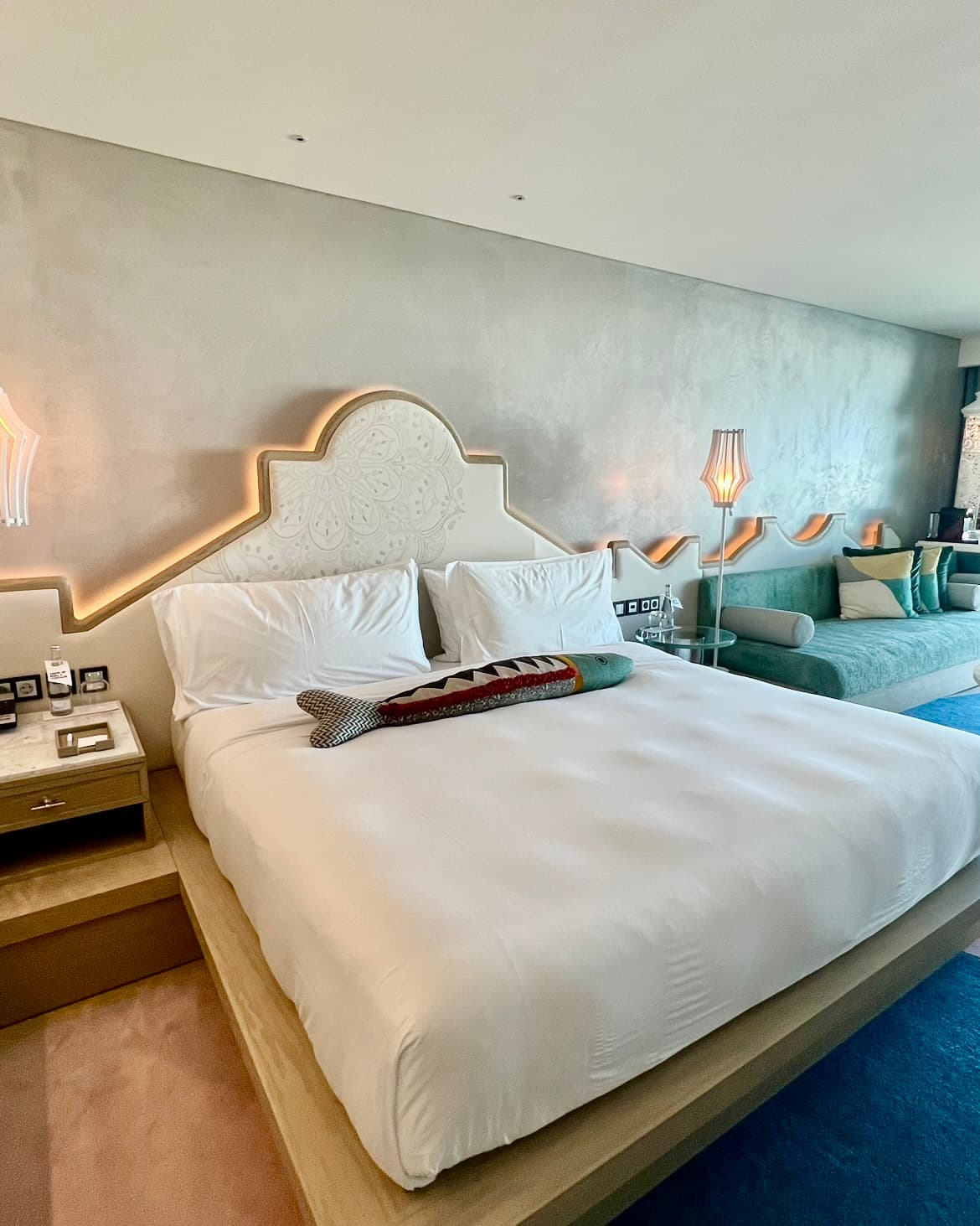 A hotel bedroom with a white bed pushed against a back wall in the center of the room