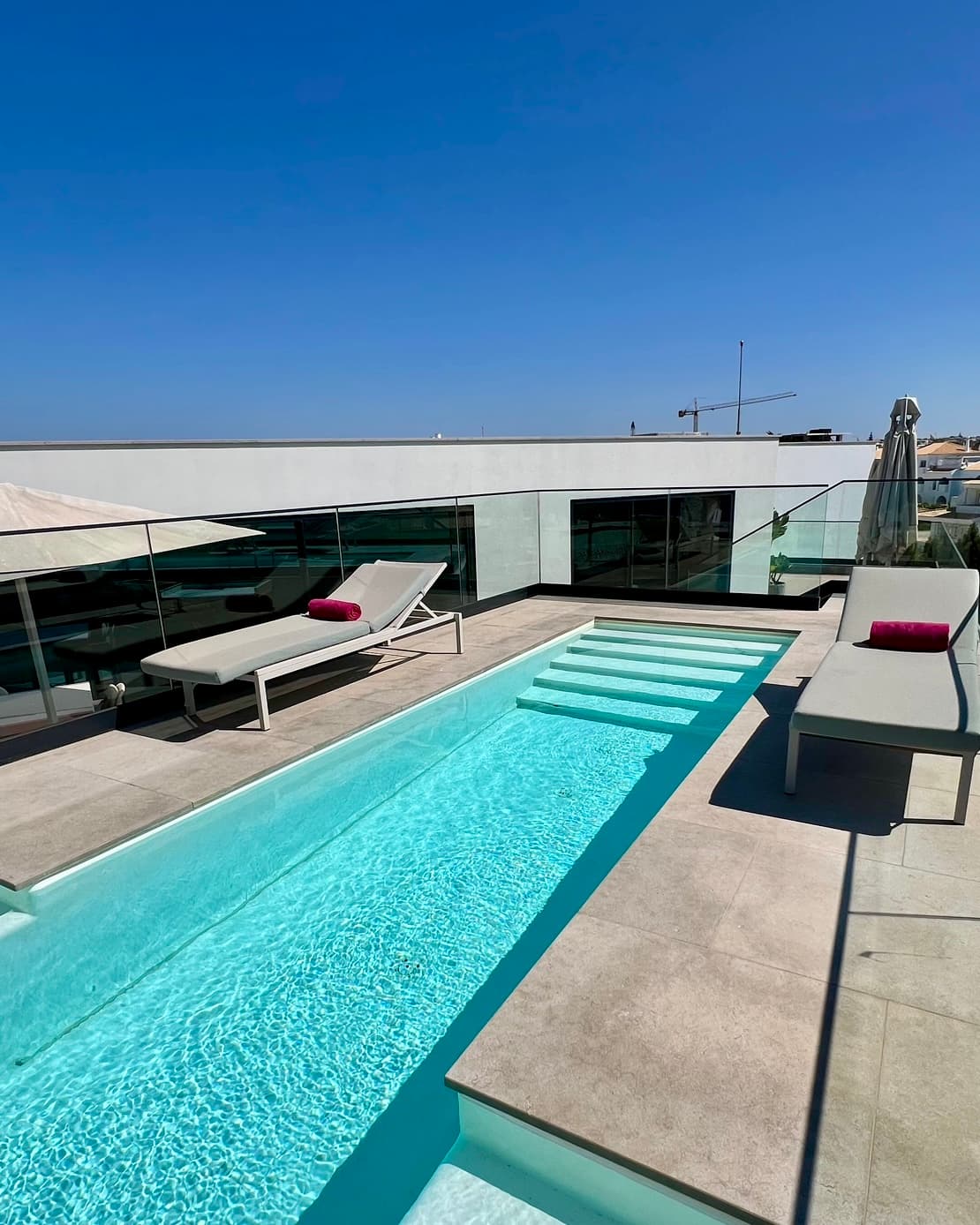 A narrow pool with two grey sunloungers either side.