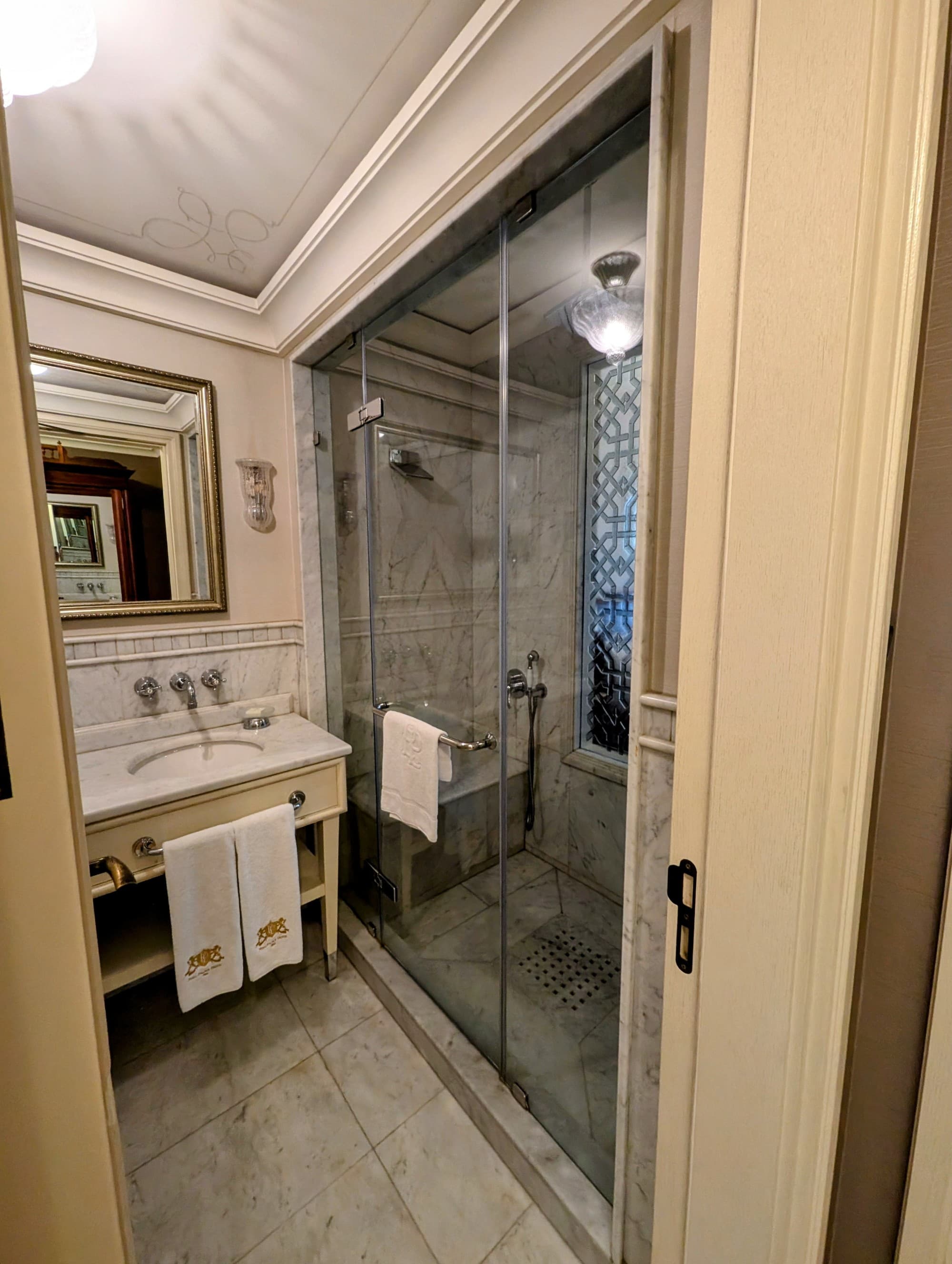 A hotel bathroom with a marble floor and glass shower doors.