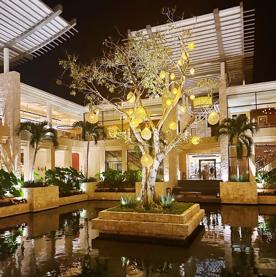 Hotel lobby interior with a tree draped in lanterns surrounded by a pool.