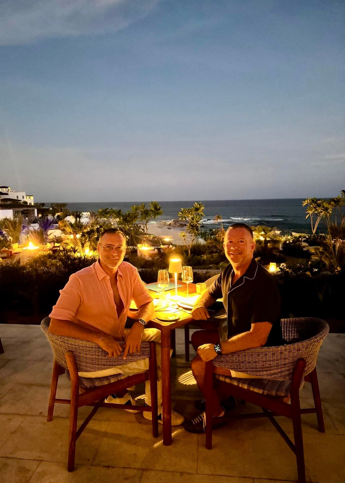 Two men dining outside at the Palmerio Restaurant at night with ocean views.