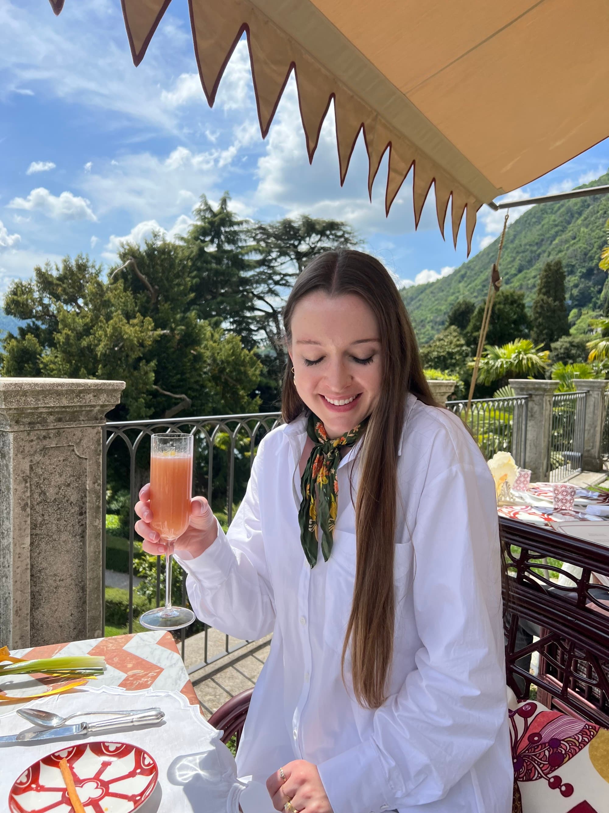 Travel advisor posing at a patio table facing the trees and sloping grass toward a mountain face.