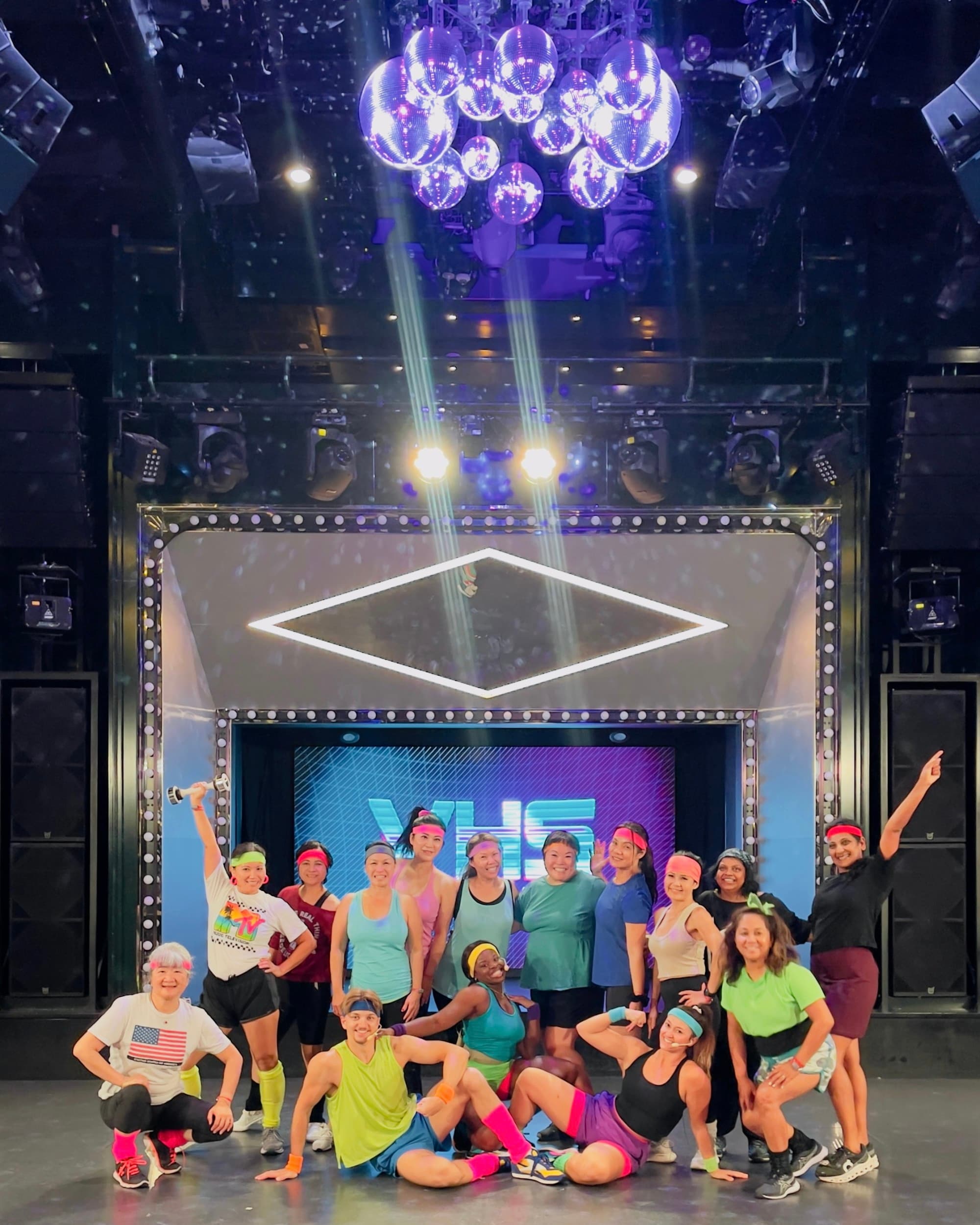 A group of women dressed in 80s workout gear in front of a photo backdrop