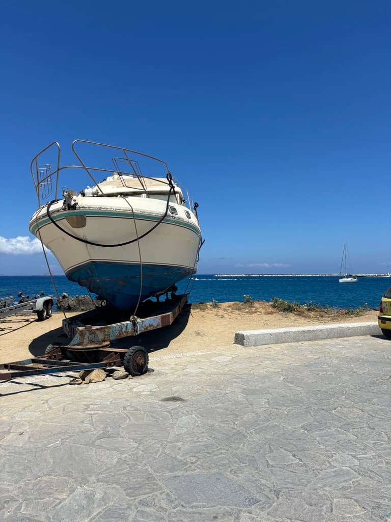 A boat out of water on the beach next to the ocean.