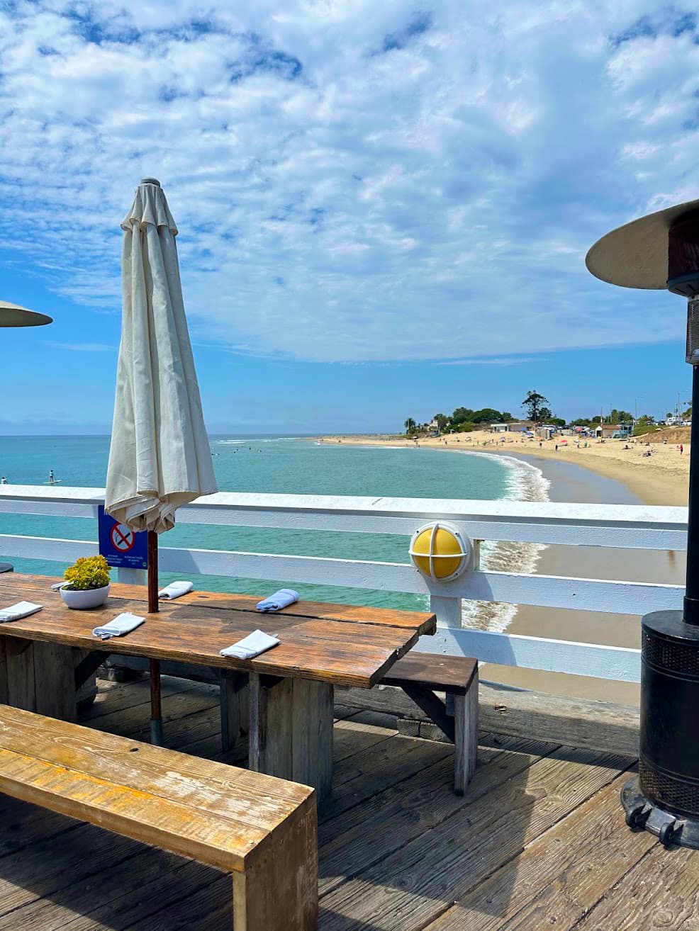 View of a wooden bench restaurant table on a deck overlooking a beautiful beach with calm waves