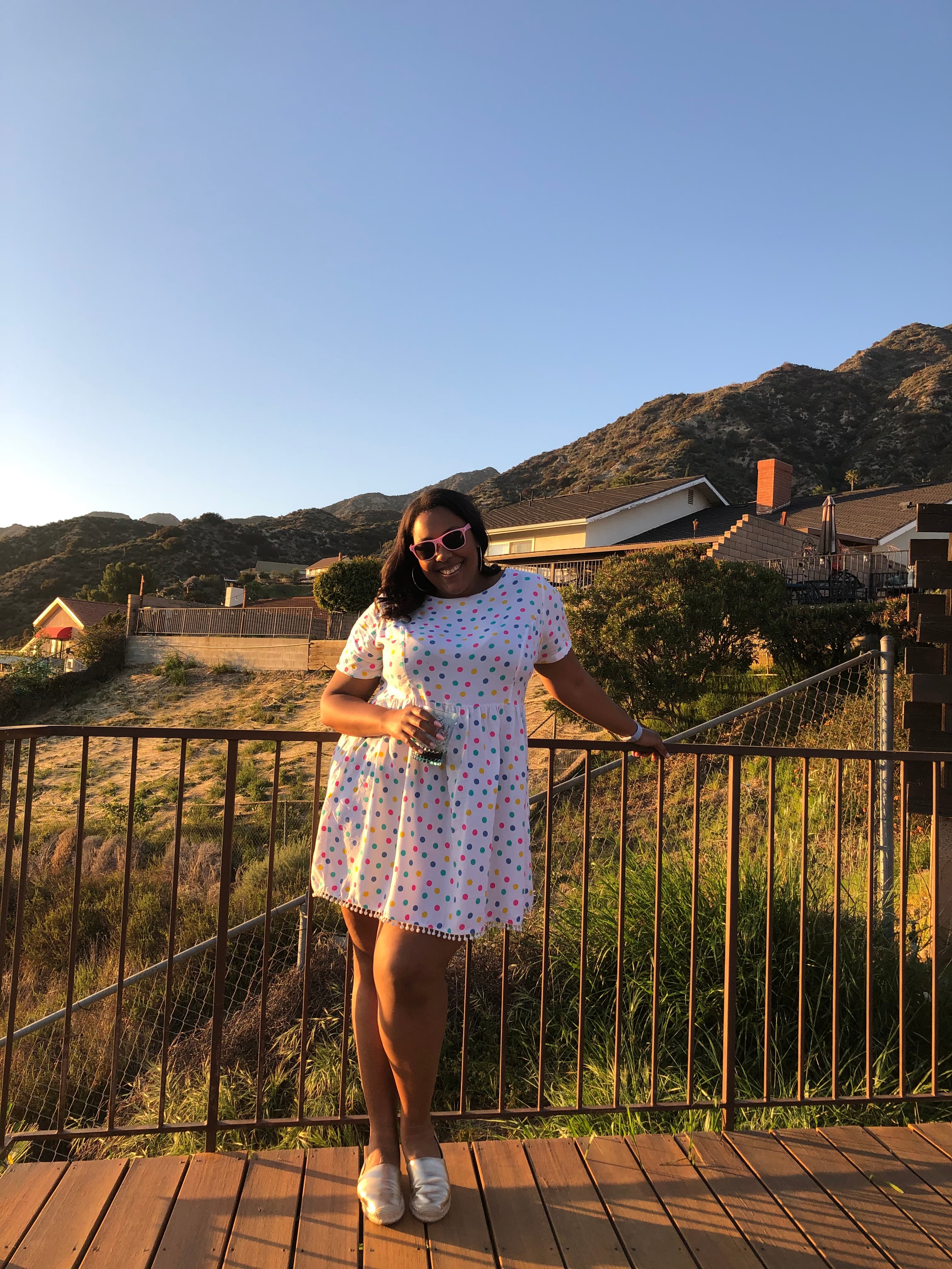 Advisor in a short white dress posing by a railing overlooking a grassy valley under clear skies