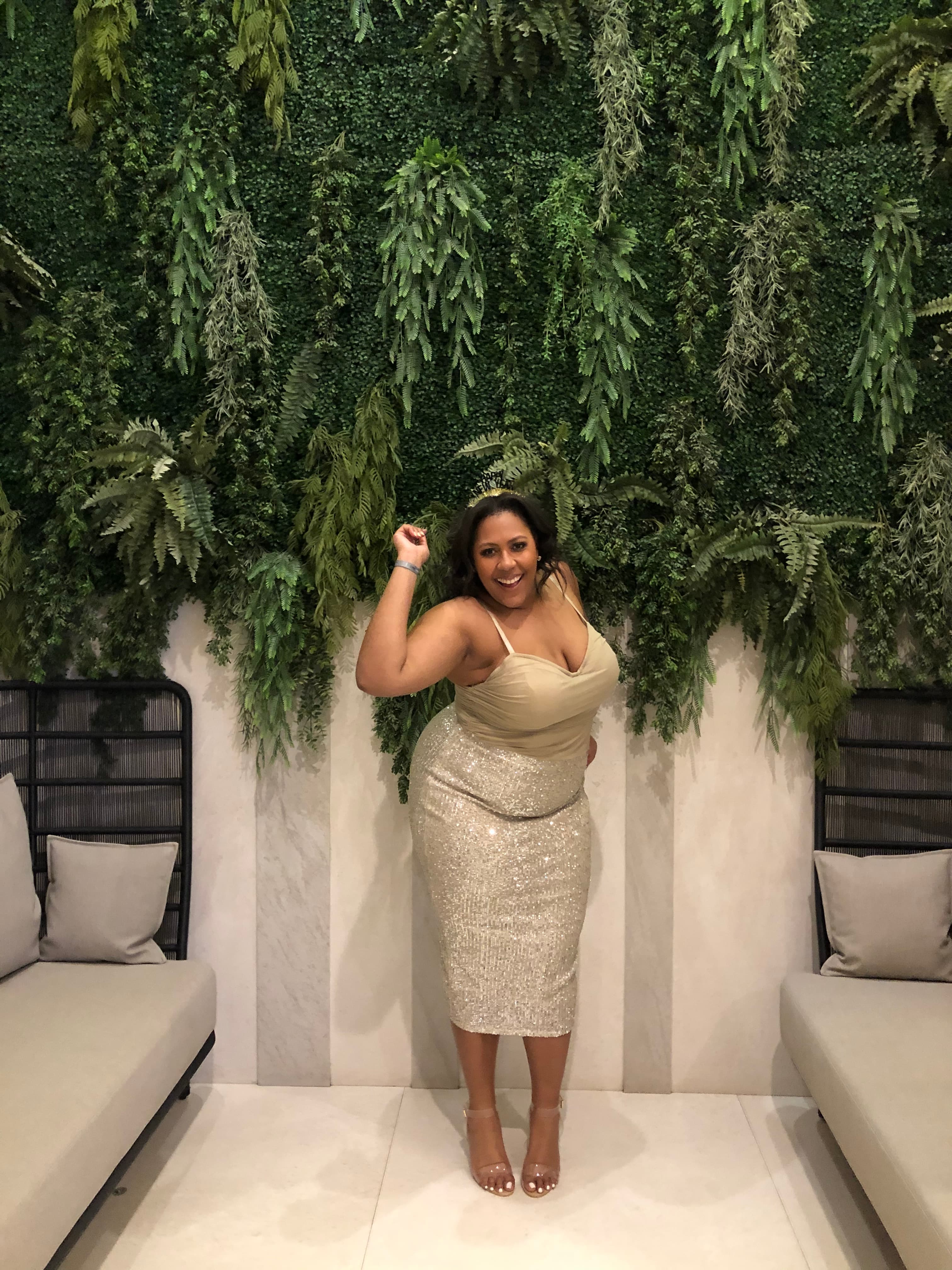 Advisor in a beige evening dress posing by an indoor wall covered in hanging plants
