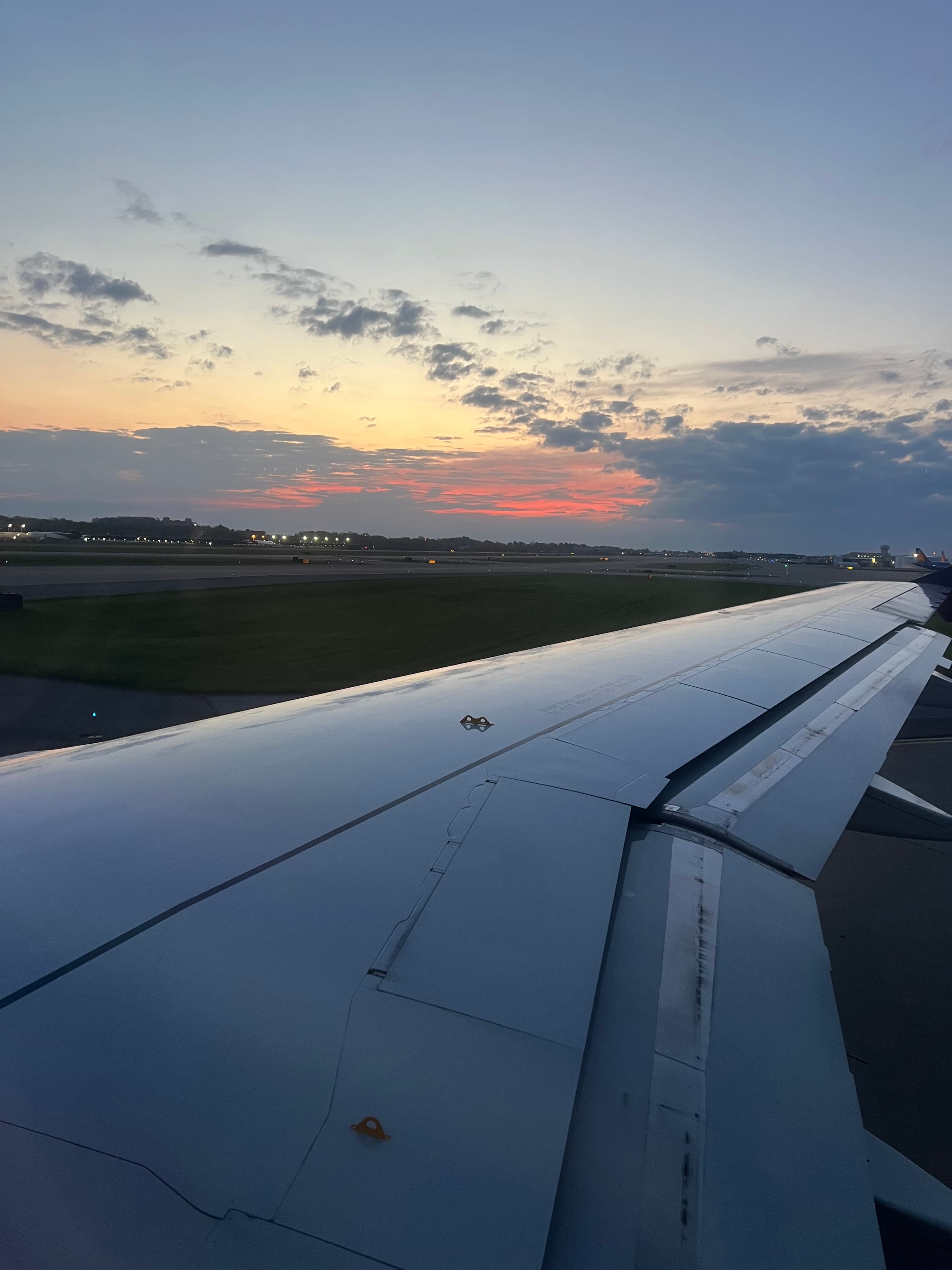 View of a plane’s wing in the sky at sunset with clouds on the horizon