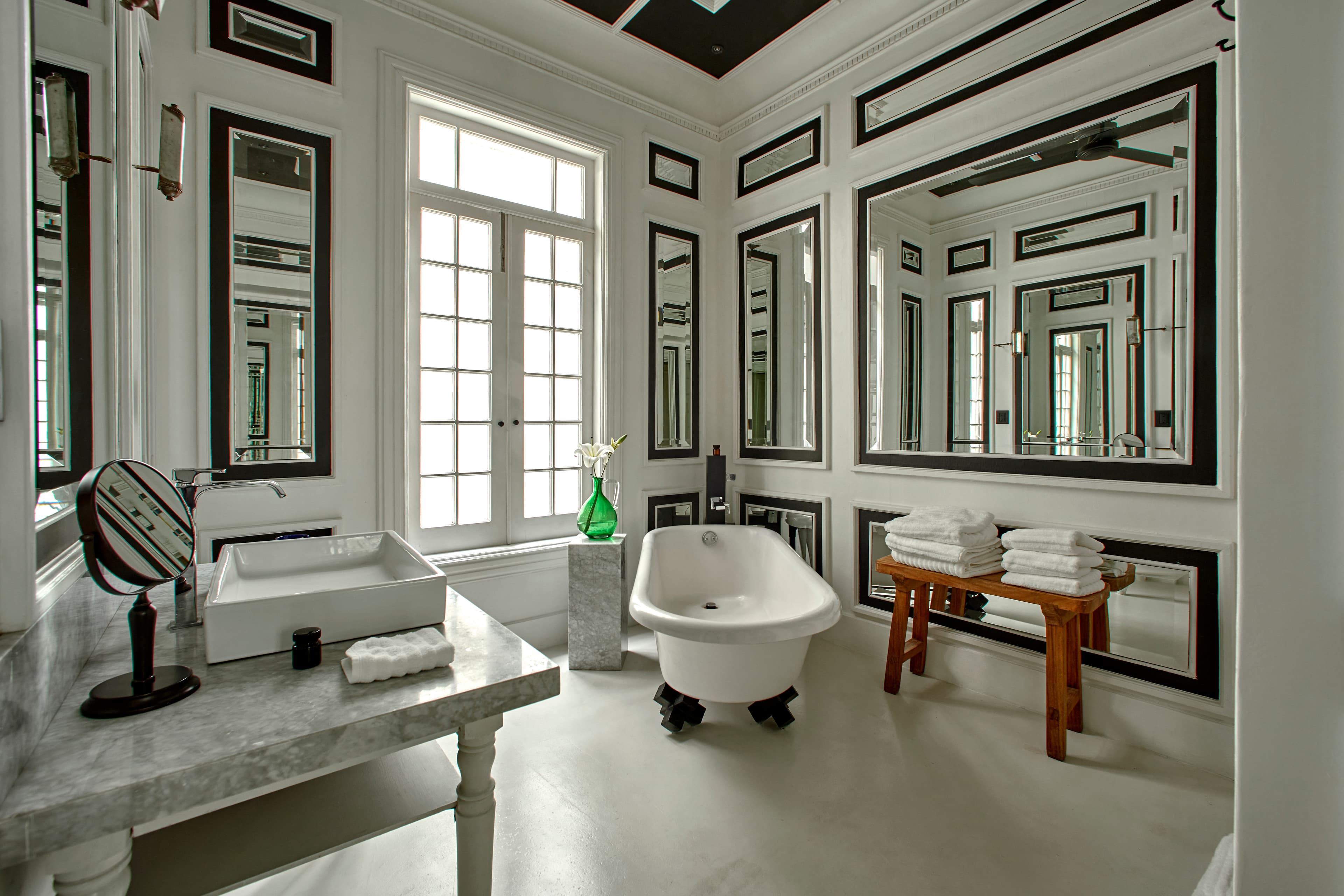A large hotel bathroom at La Valise Mexico City with white interiors, a standalone bathtub and large wall mirrors with black rims.