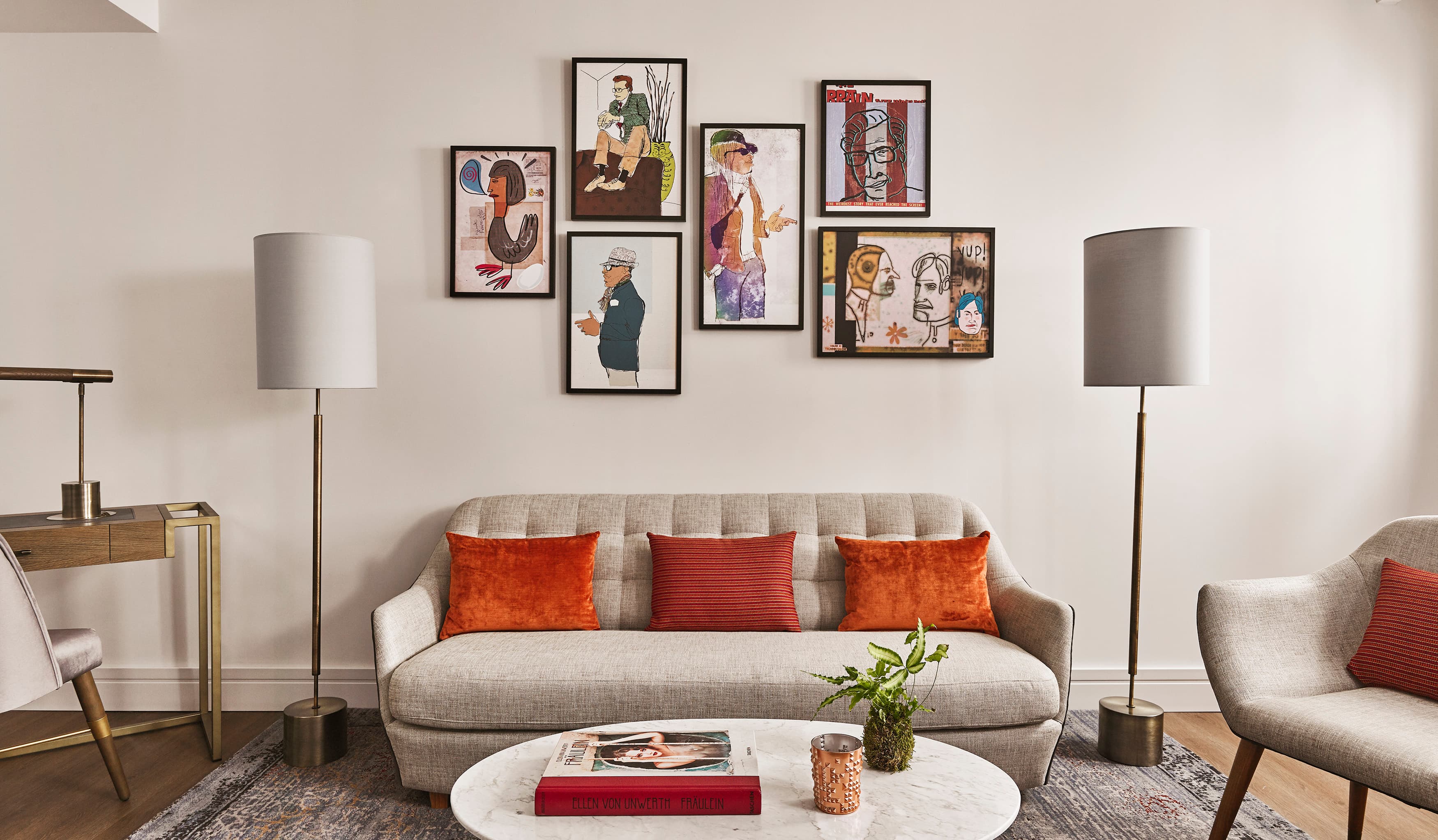 A view of an elegant living room area with grey armchair and chair and grey floor lamps, colorful artwork on the wall.