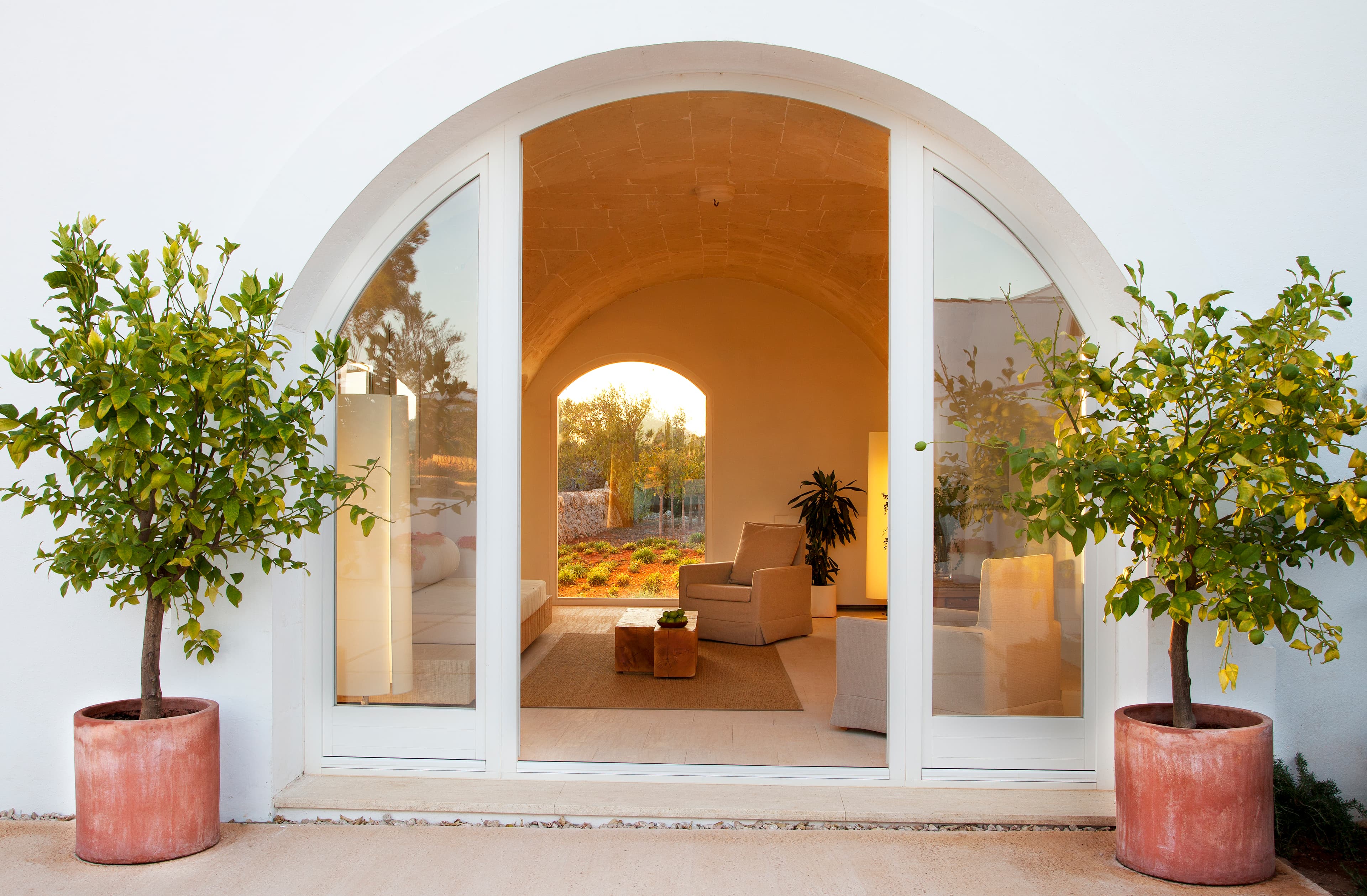 A white arched entrance to a hotel room with terracotta plant pots either side with a sleek, neutral interior.