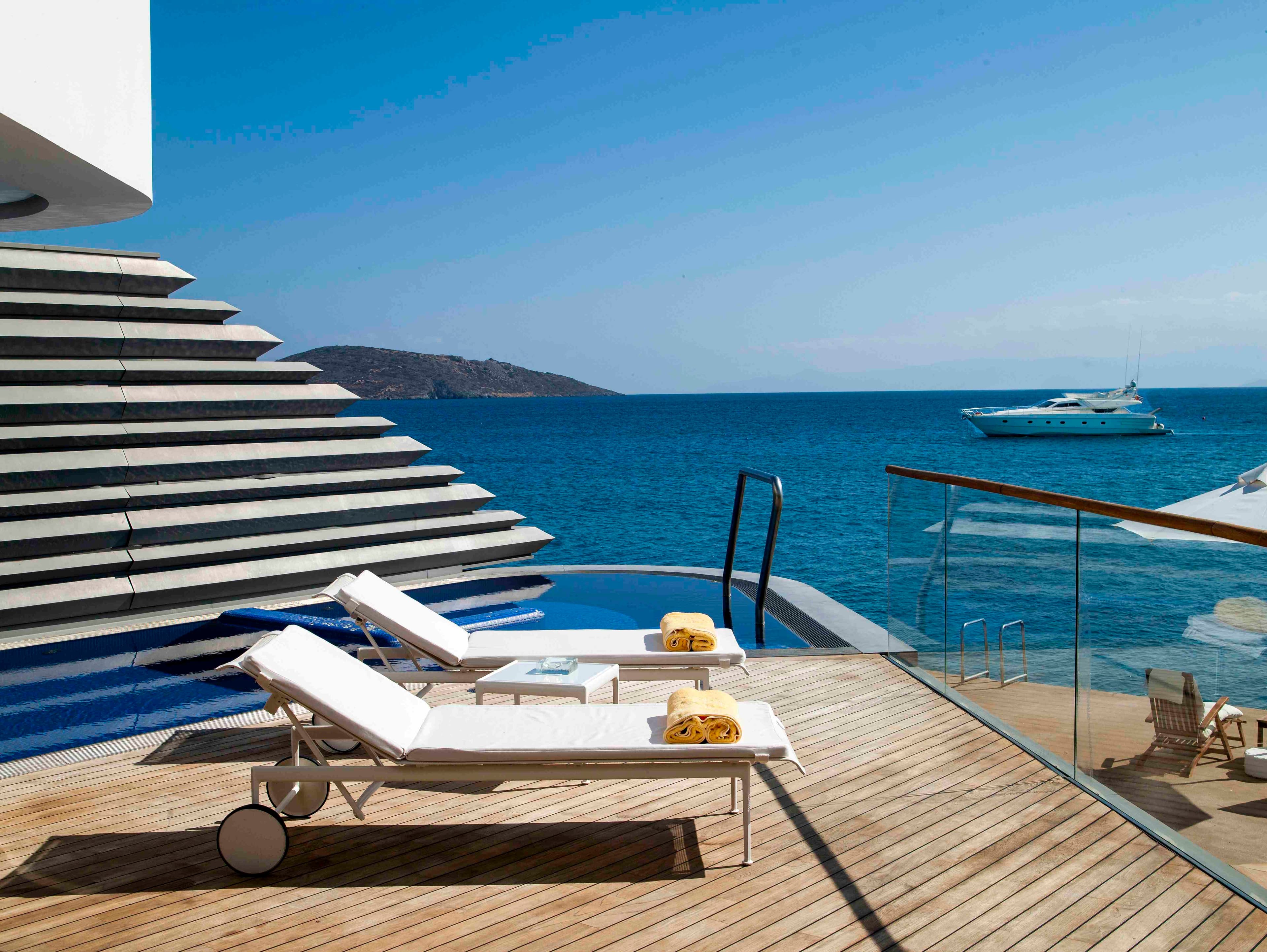 A view of a deck with sun loungers and a glass balcony, private pool and ocean views.