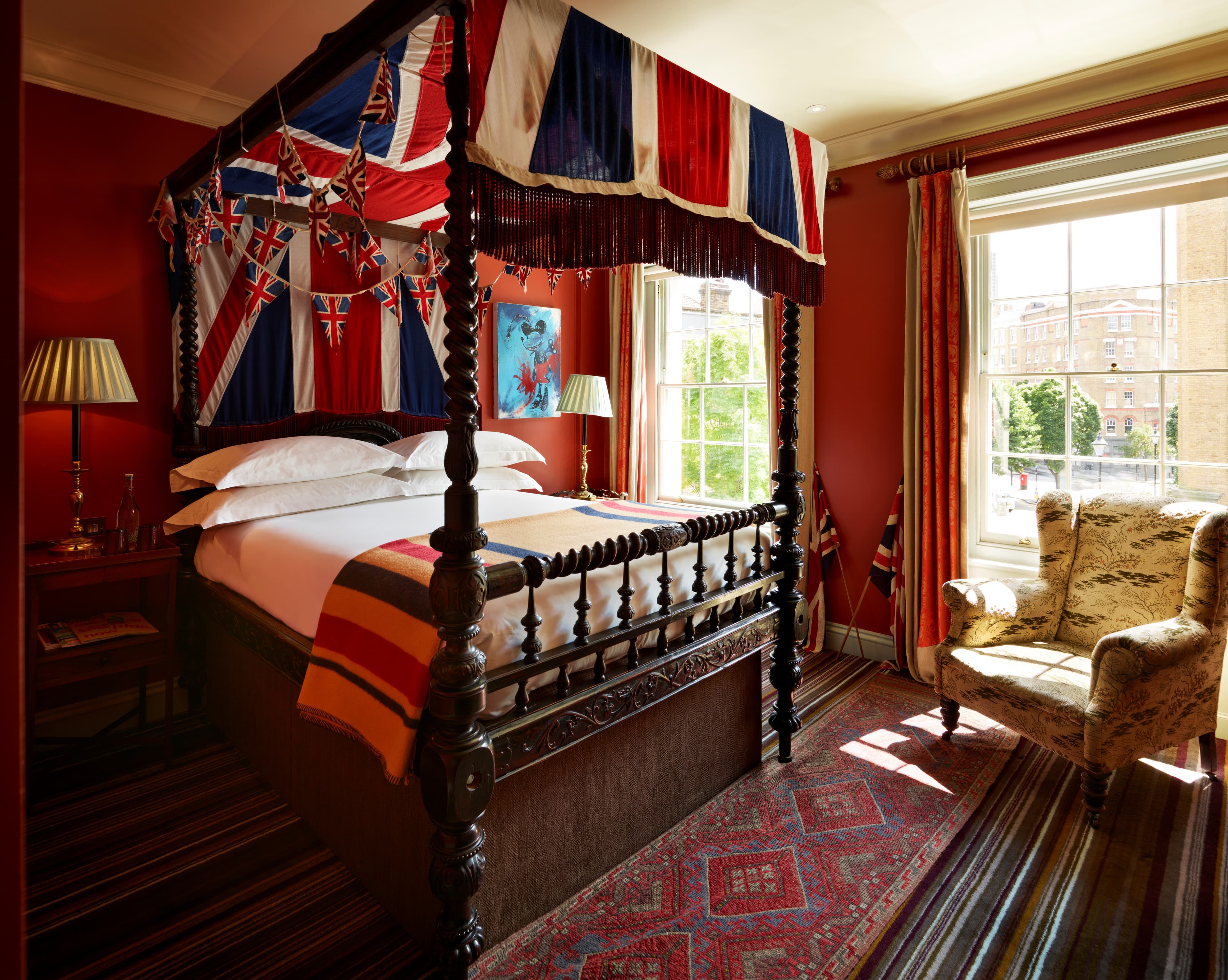 A hotel room with a four poster bed and a hanging UK flag and dark red walls and rug.