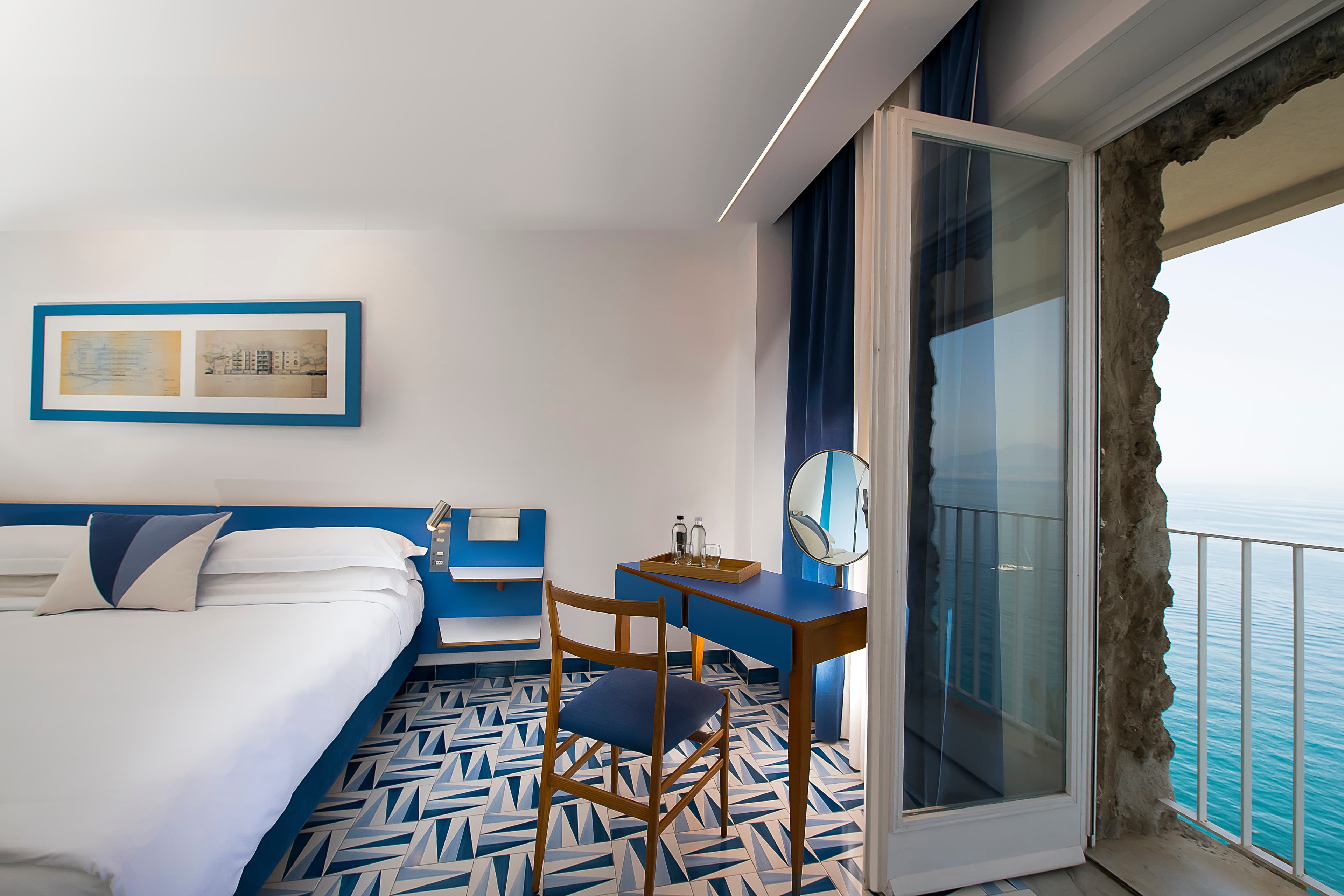 A hotel room with blue and white decoration and an open door with balcony and sea view.