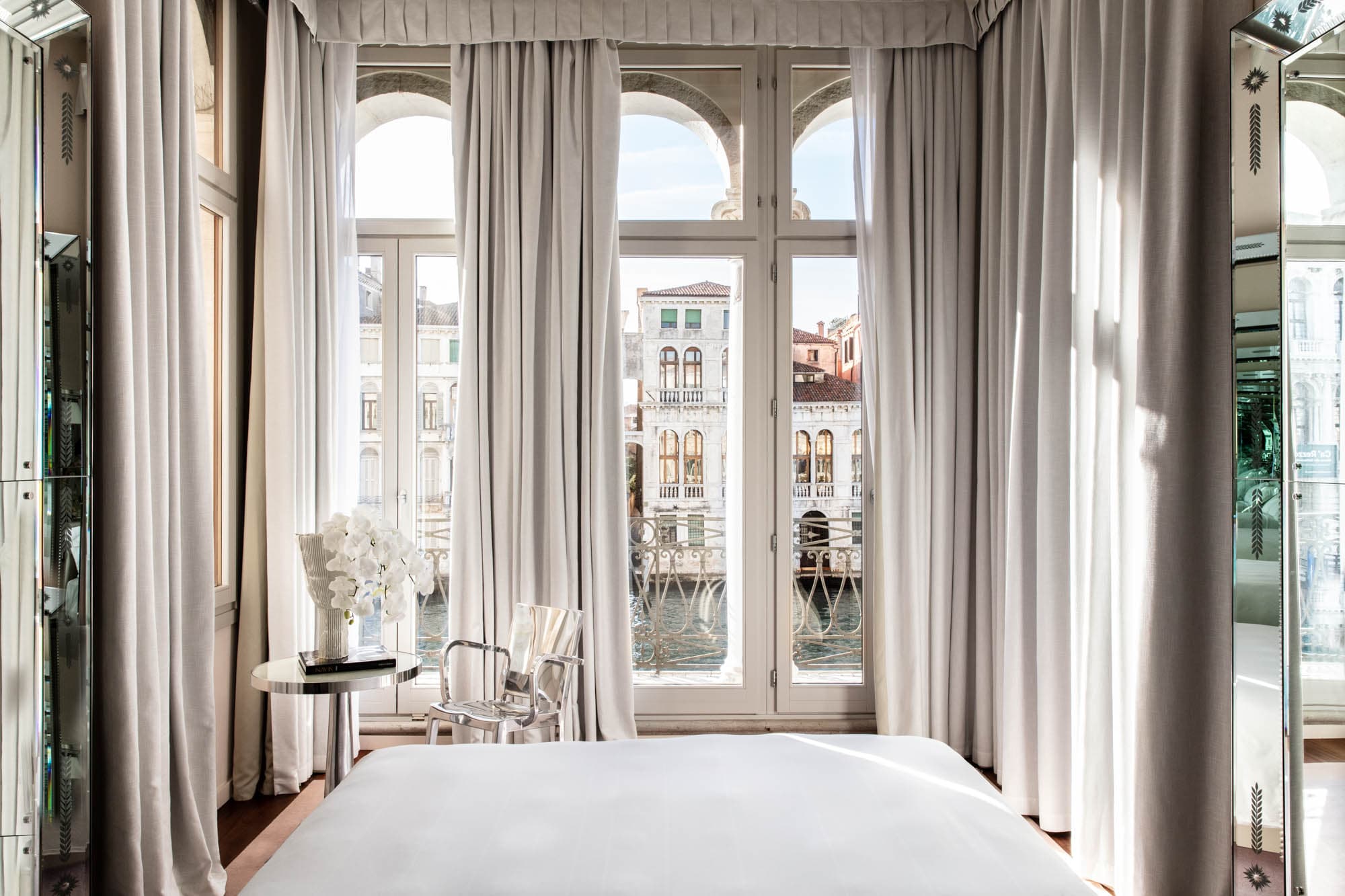 A view of a hotel room with white and chrome tones overlooking the canal in Venice.