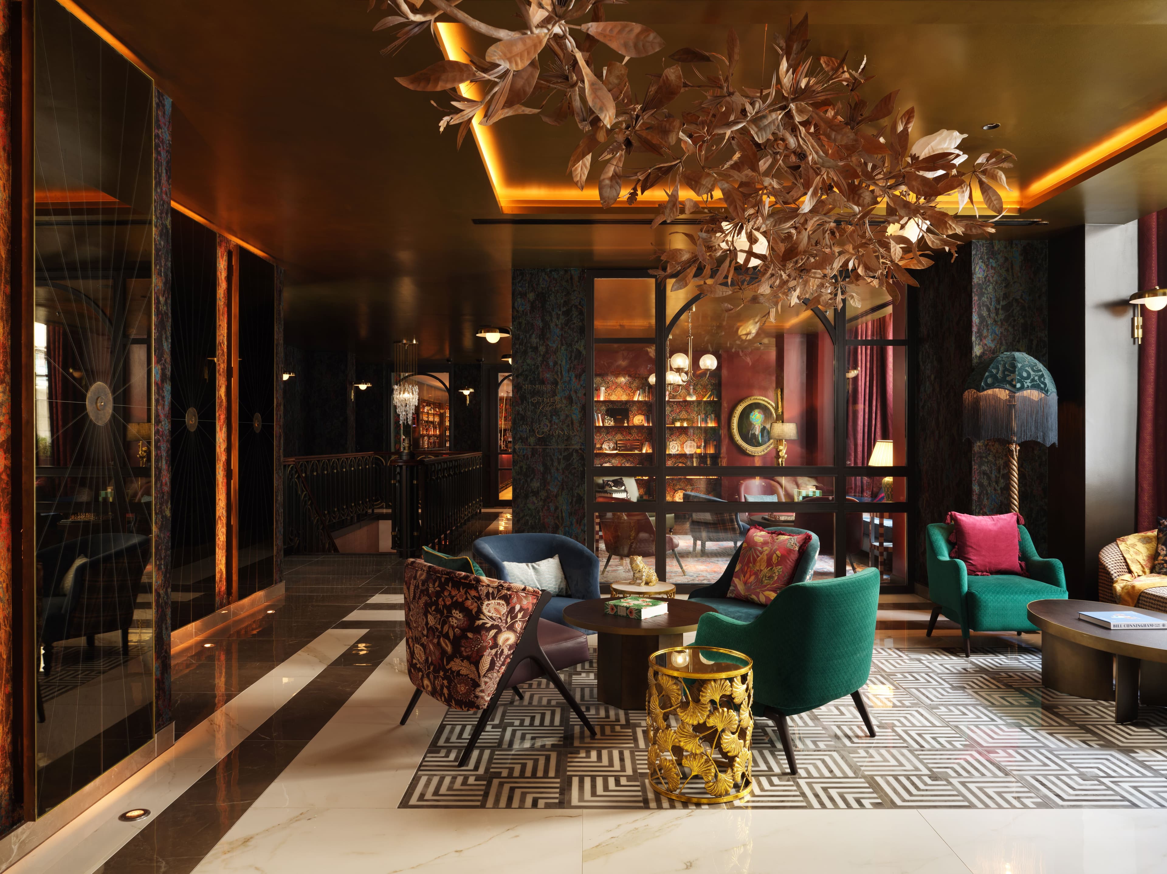 A stylish lobby and lounge area of a hotel with plush armchairs and warm lighting and eclectic decoration.