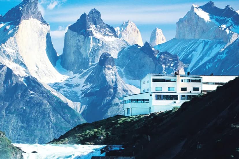 a white hotel on a cliff overlooking an icy alpine lake