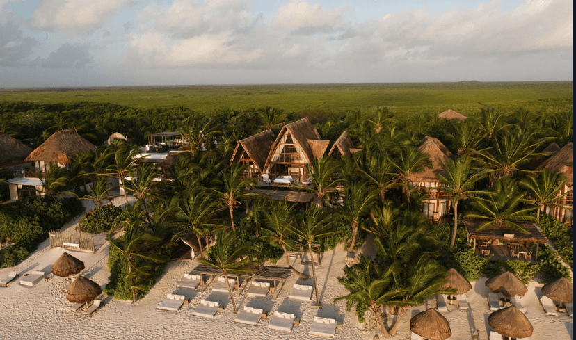 An aerial view of La Valise Tulum with palapa-stye huts scattered around the beach and forest.