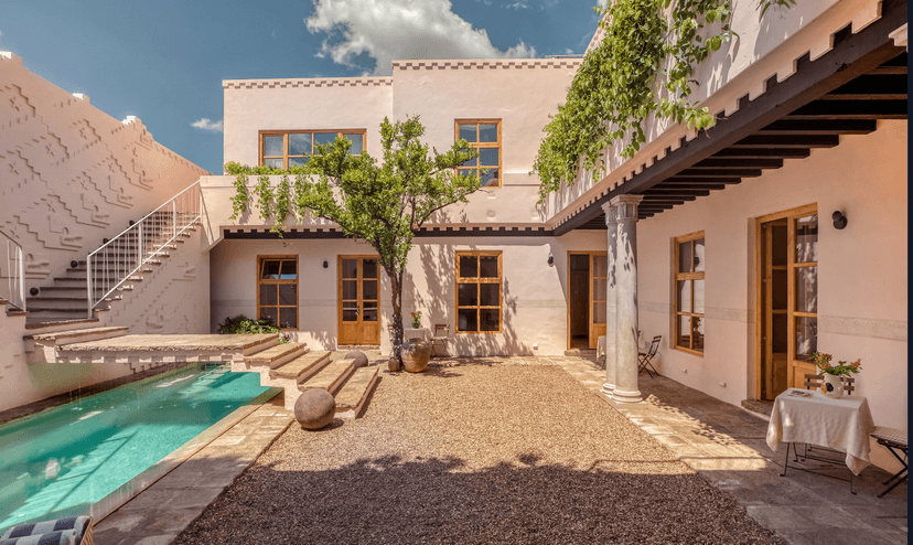 The image shows an outdoor couryard with a pool and surrounding pink buildings at La Valise San Miguel de Allende.