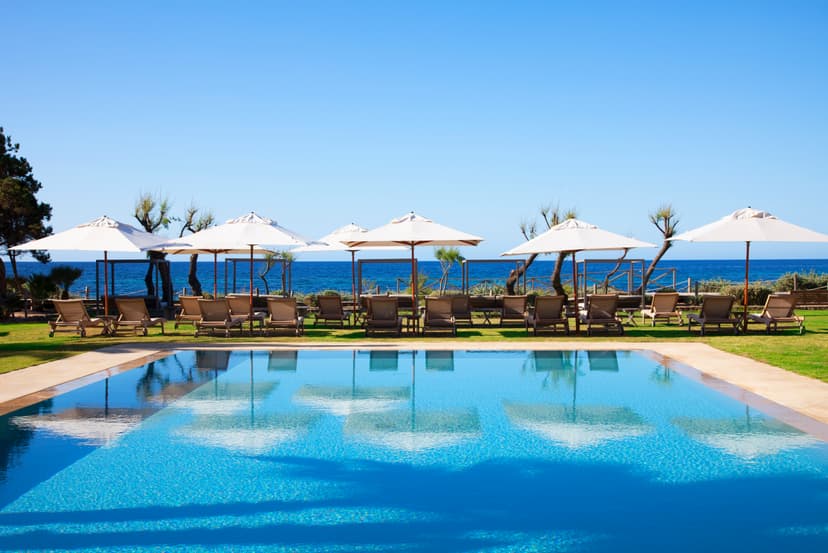 A view of a pool area surrounded by grass and sun loungers looking out towards the ocean.