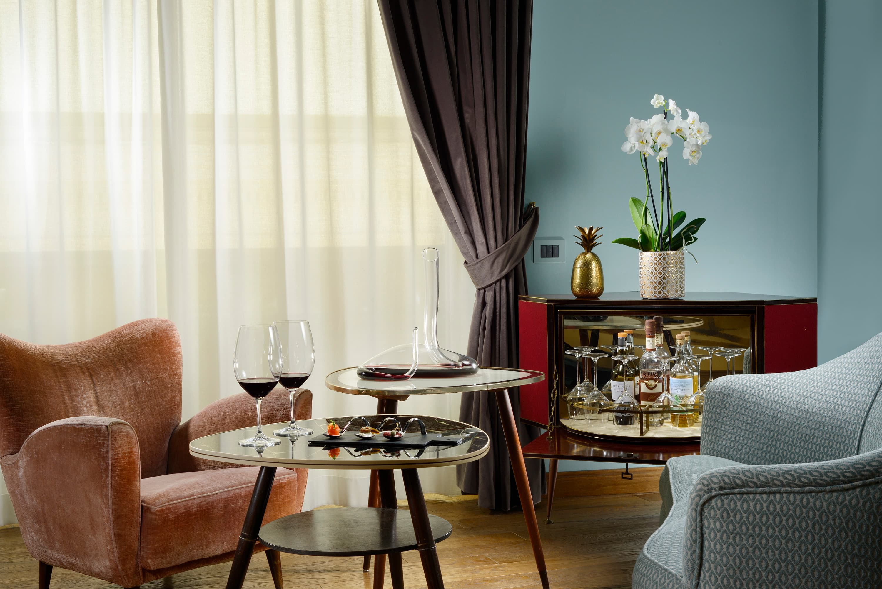 A blue painted room with two lounge chairs facing a small table with two glasses of wine and a decanter.