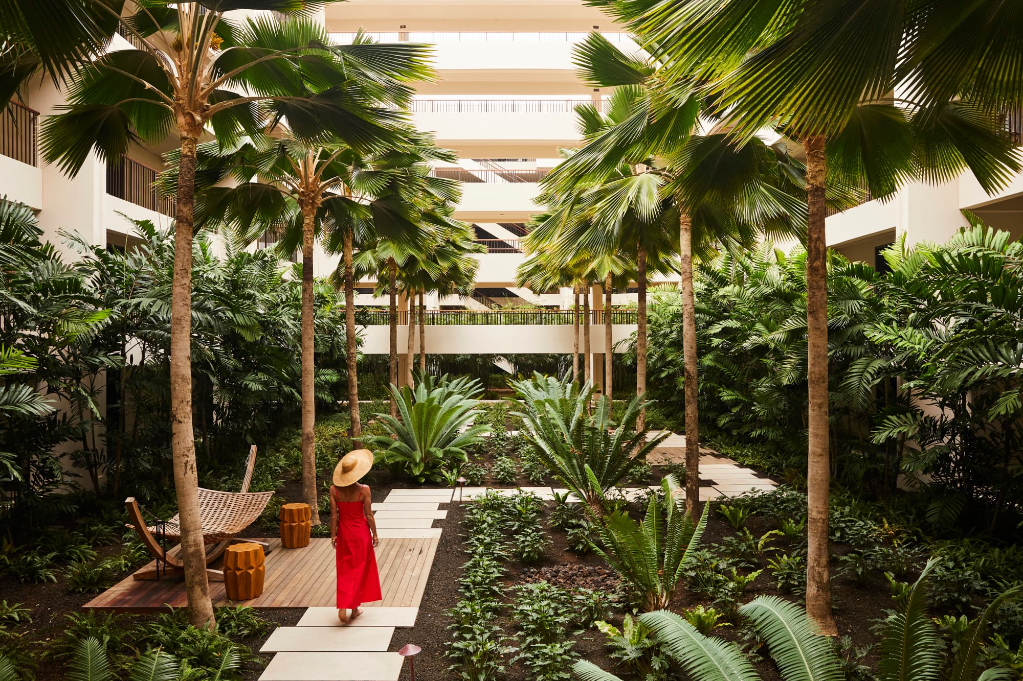 woman in red dress and sunhat walking in a hotel courtyard garden