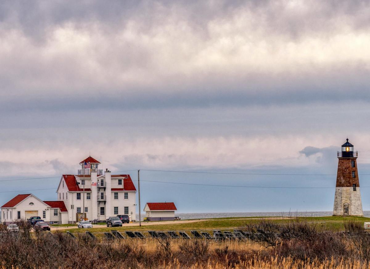 Lighthouse besides mansion by the ocean in Rhode Island on a cloudy day.