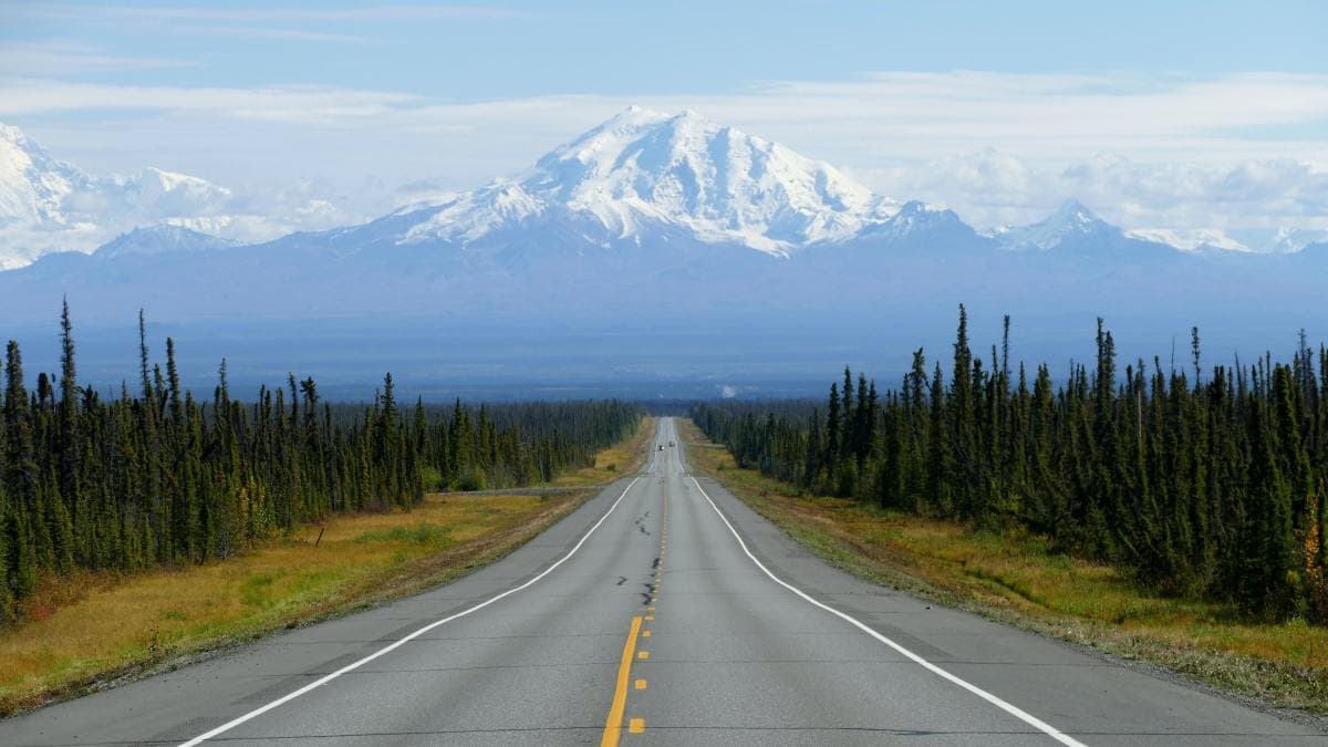 Wide road stretching to snowy mountains in Alaska.