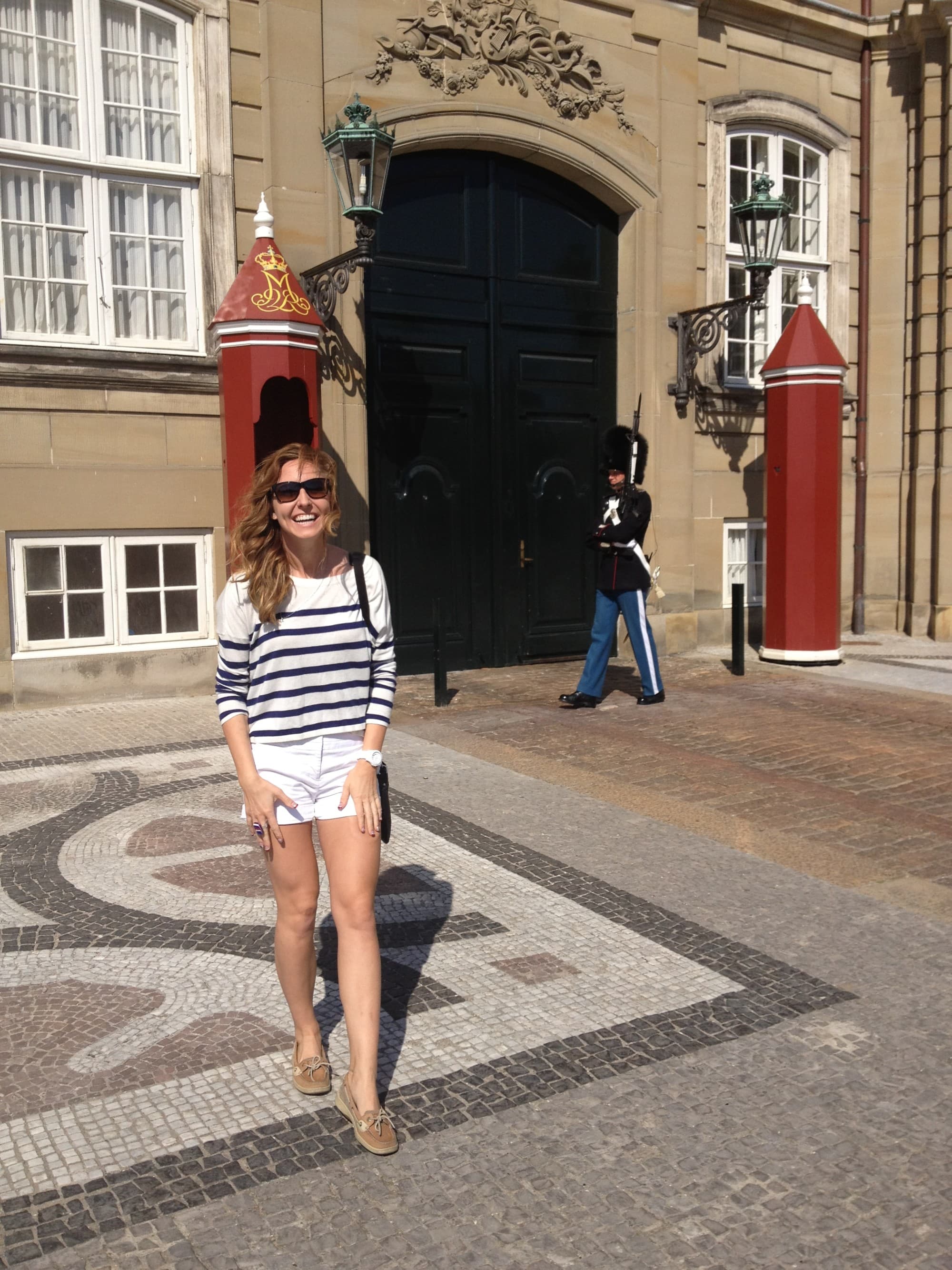 a woman in a striped shirt and white shorts stands in front of an old building