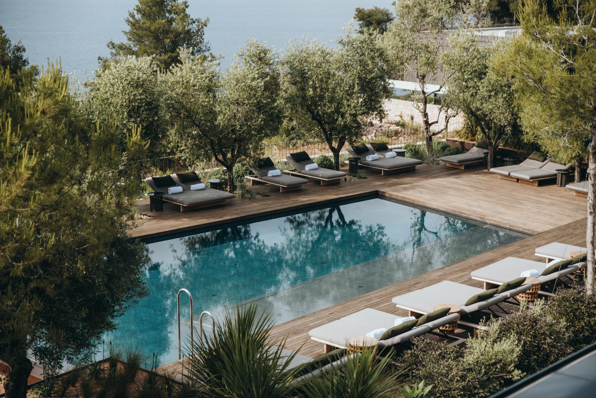 a seaside wooden pool deck surrounded by lounge chairs and trees