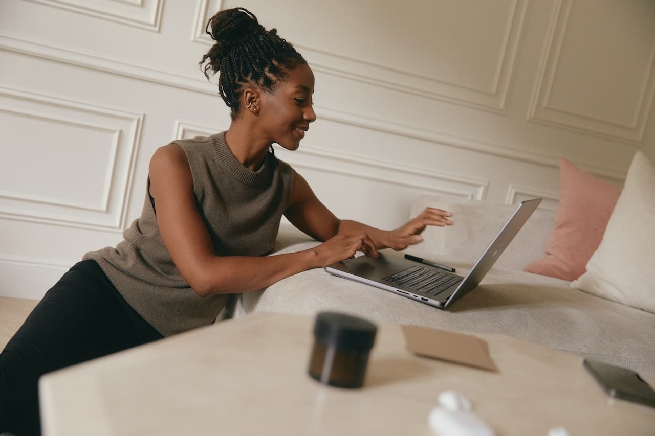 a woman in a gray sweater works on her laptop in a white room