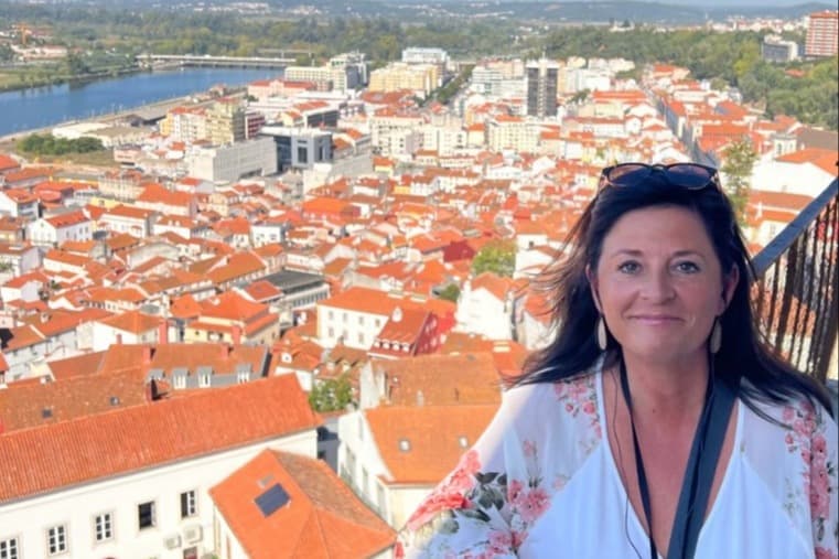 a woman stands on a balcony overlooking red-tiled buildings
