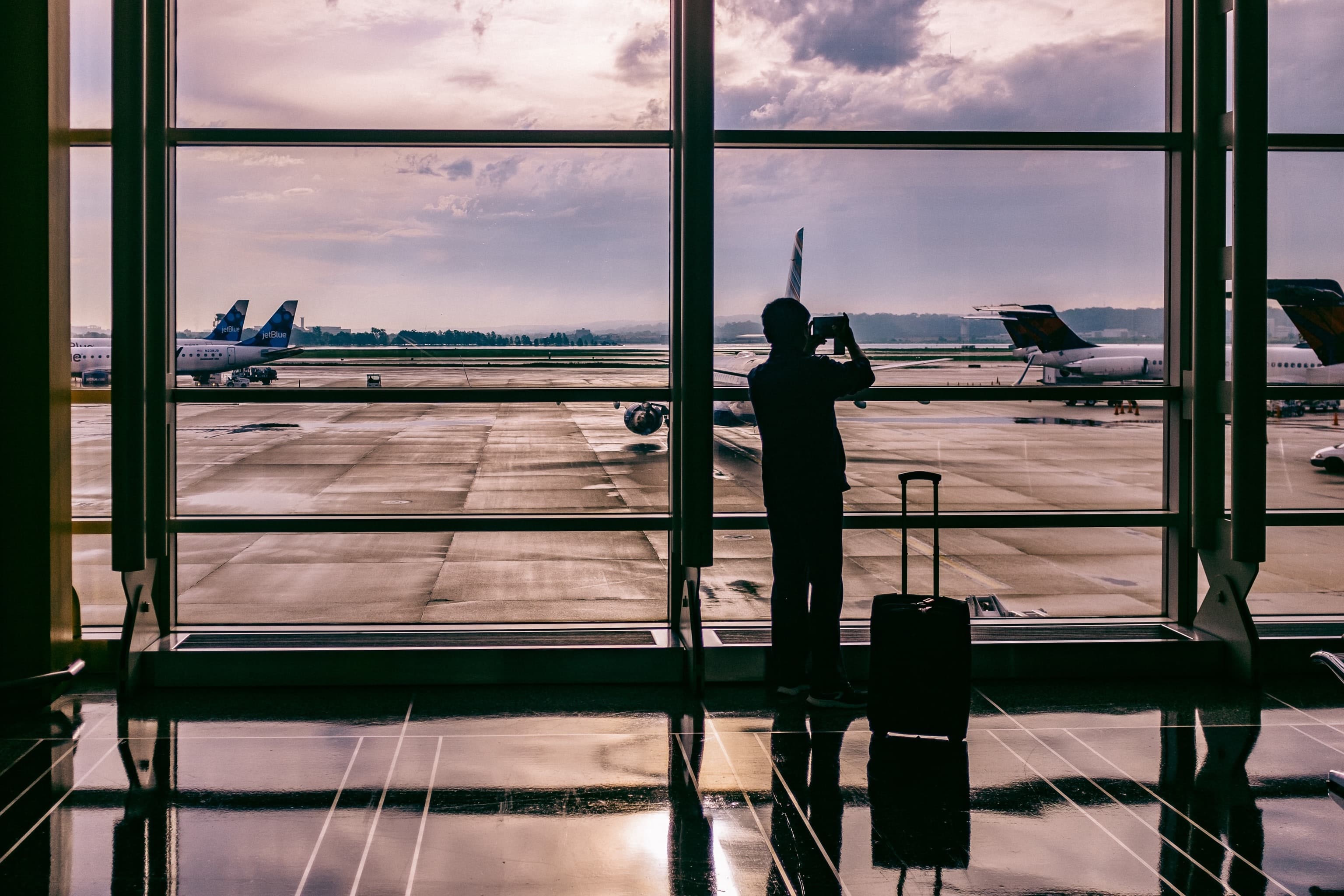 Man at airport with suitcase taking picture of planes