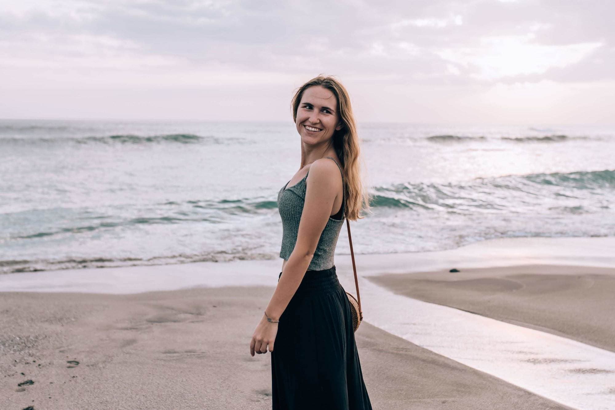 a woman in a tank-top and black pants stands on a beach
